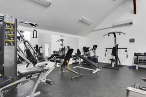 Dedicated fitness area featuring rubber flooring, mirrored wall, and vaulted ceiling