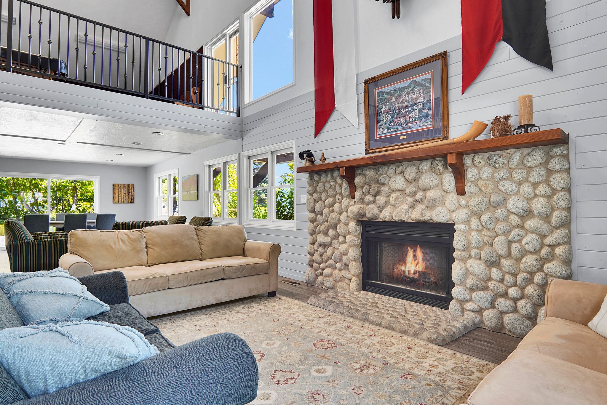 Great room featuring a river rock fireplace with a wood mantle, vaulted ceilings, and a second-story interior balcony with metal railings