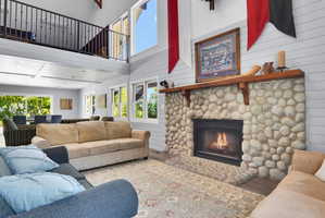 Great room featuring a river rock fireplace with a wood mantle, vaulted ceilings, and a second-story interior balcony with metal railings