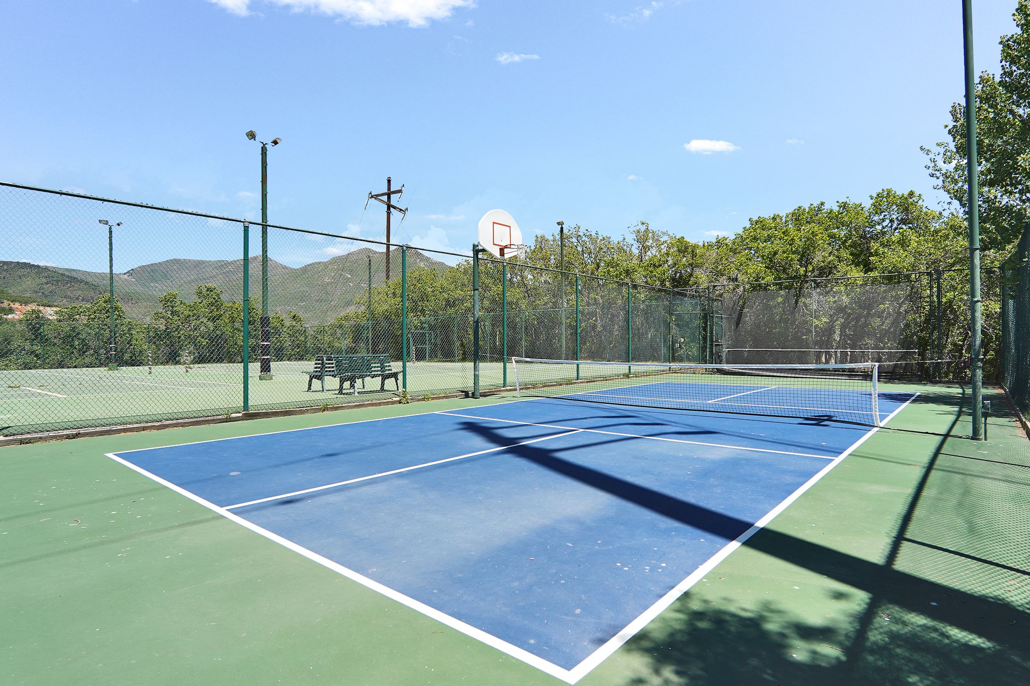 Pickleball court featuring a surface with white boundary lines.  Tennis courts in the background (under repari)