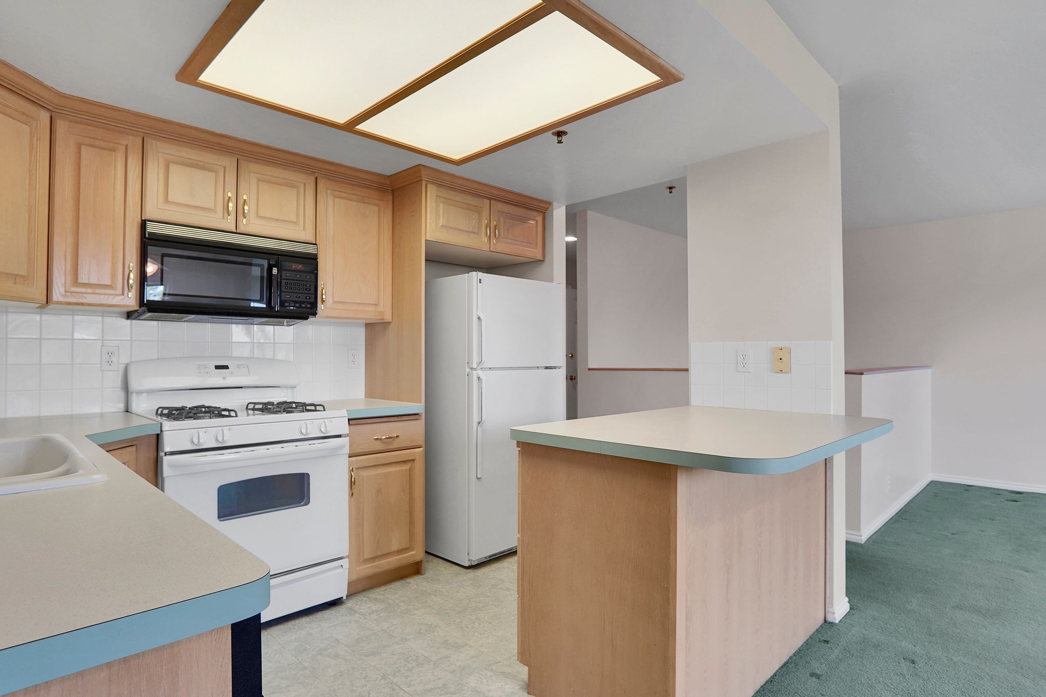 Kitchen featuring wood-finish cabinetry, white tile backsplash, and light-toned countertops with blue trim