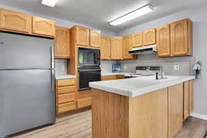Kitchen featuring wood-finish cabinetry, tile countertops, stainless steel refrigerator, built-in microwave, and wood-finish flooring