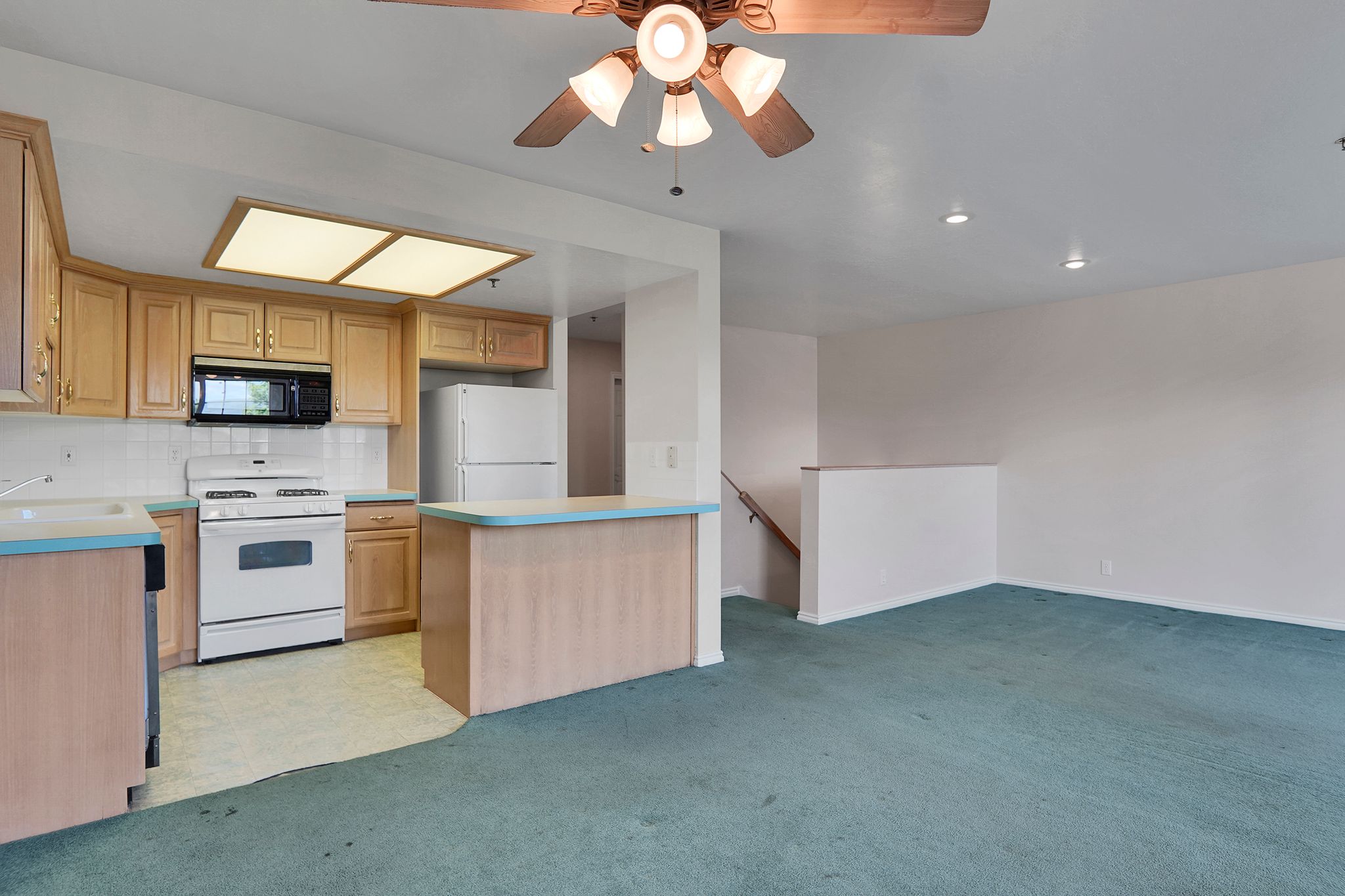 Kitchen featuring natural wood-finish cabinetry, white tile backsplash, a white electric range, and a breakfast bar with light blue countertops