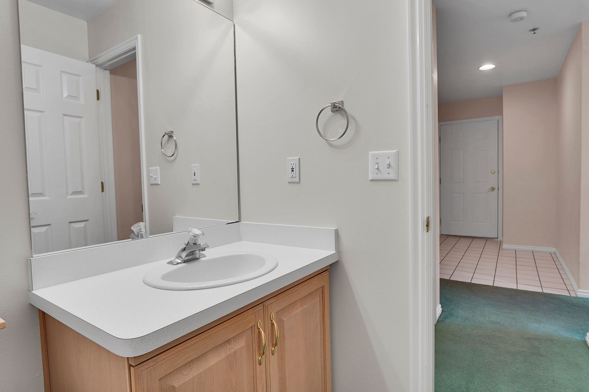 View of Entry way from Bathroom vanity featuring light wood cabinetry, a white countertop with an integrated sink, and a large wall-mounted mirror