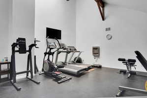 Dedicated fitness area featuring high ceilings, exposed architectural beams, durable rubber flooring, a mounted television, and a built-in water fountain