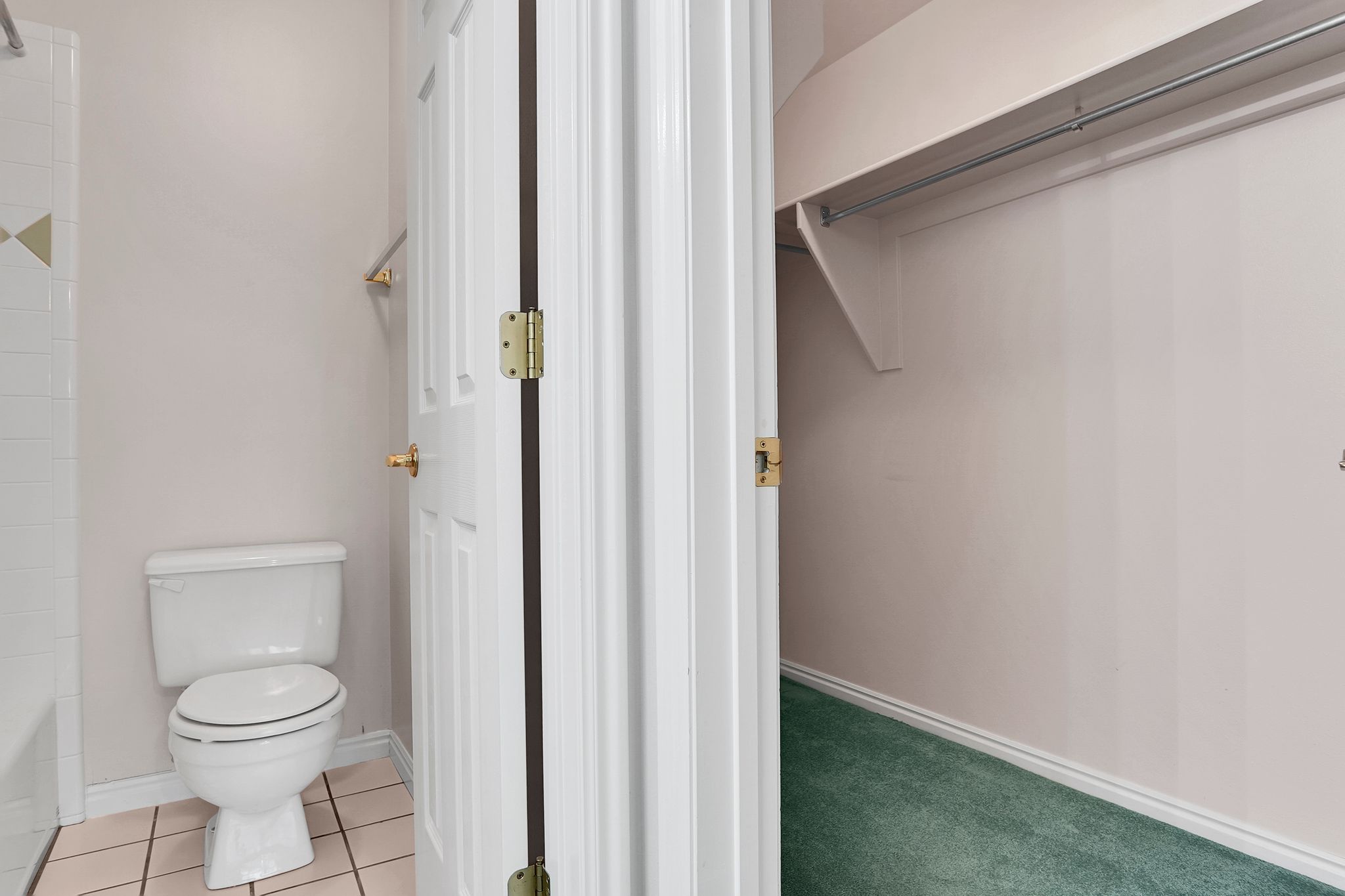 Bathroom with a white toilet, light-toned wall paint, and beige tile flooring
