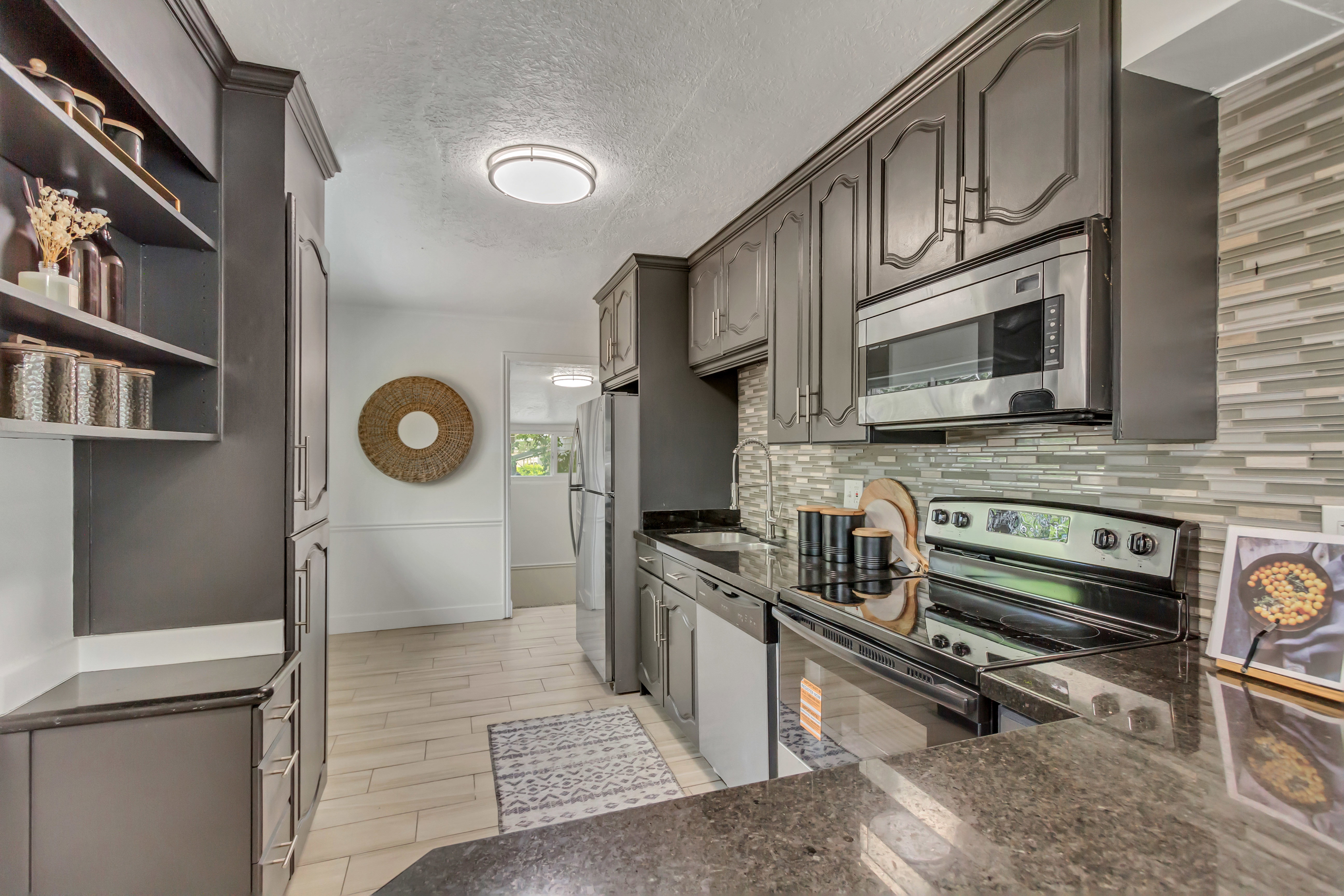 Galley kitchen featuring dark cabinetry, stainless steel appliances, a mosaic tile backsplash, wood-finish flooring, and ample counter space