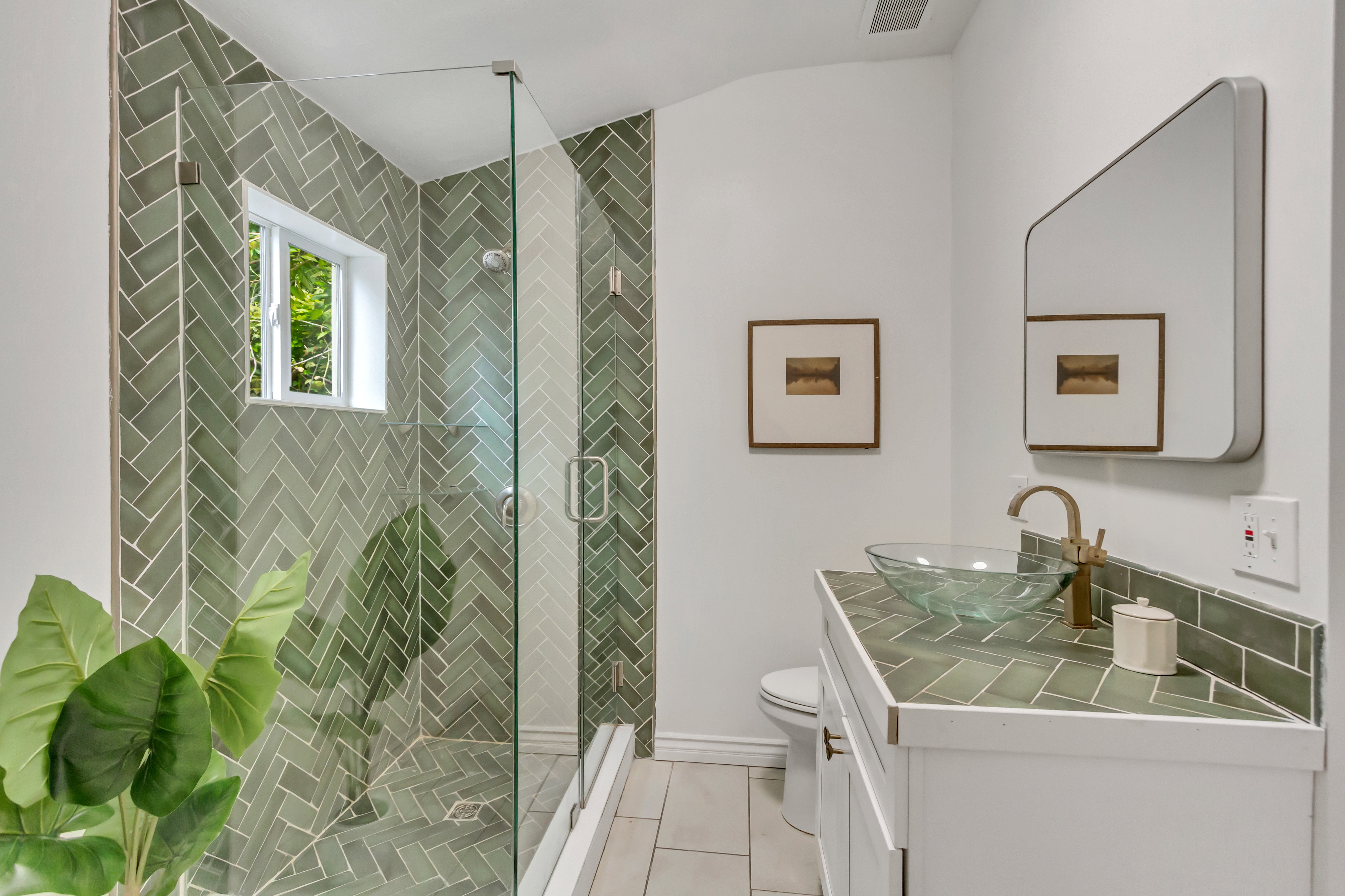 Shower enclosure with glass paneling, green herringbone tile, and a frosted window