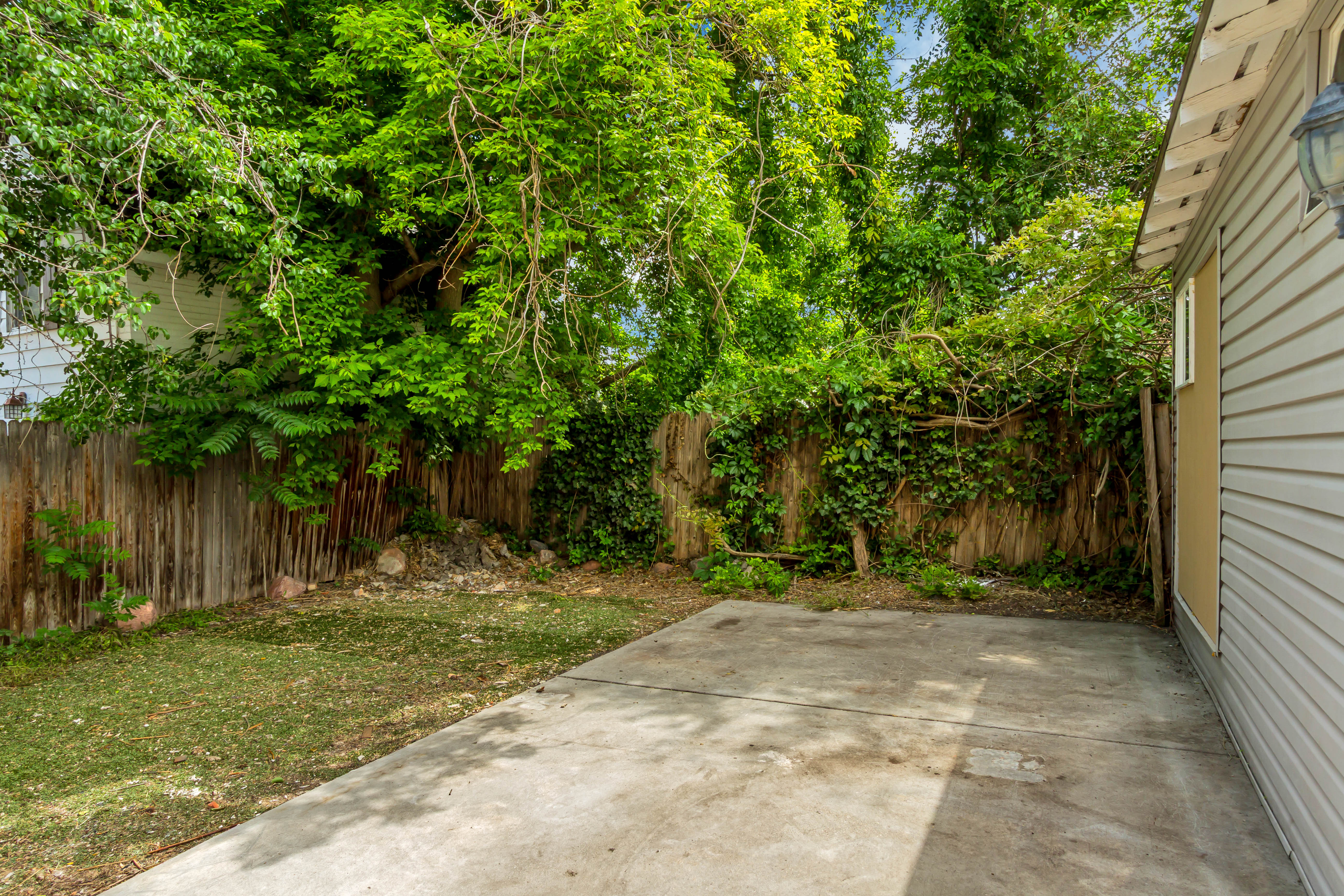 Outdoor concrete patio area featuring a patch of grass and a wood fence