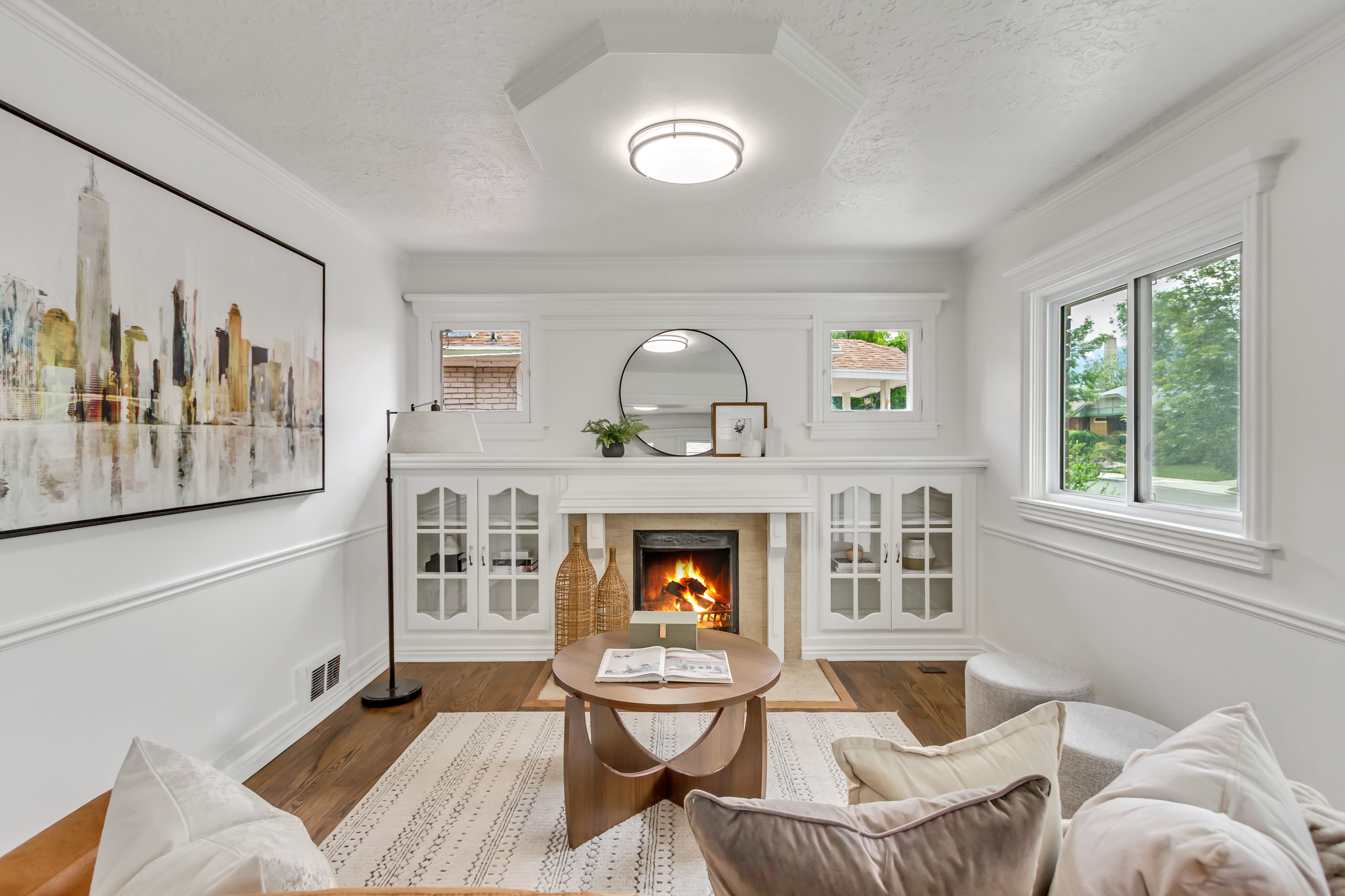 Bright living area featuring a fireplace with stone surround, custom built-in cabinetry, wood-finish flooring, white trim work, and crown molding