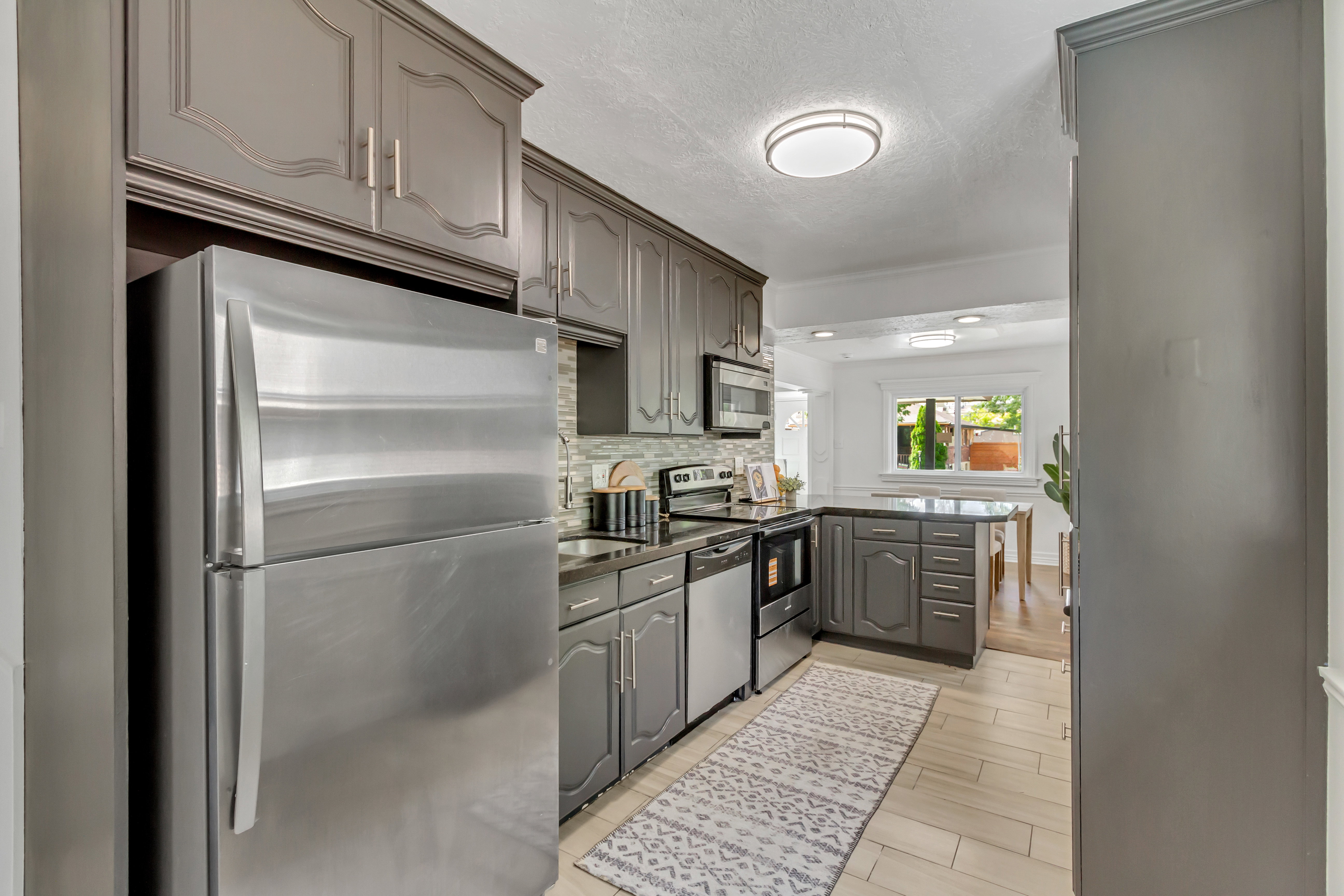 Kitchen featuring gray cabinetry, stainless steel appliances, a tile backsplash, dark countertops, and light-colored flooring