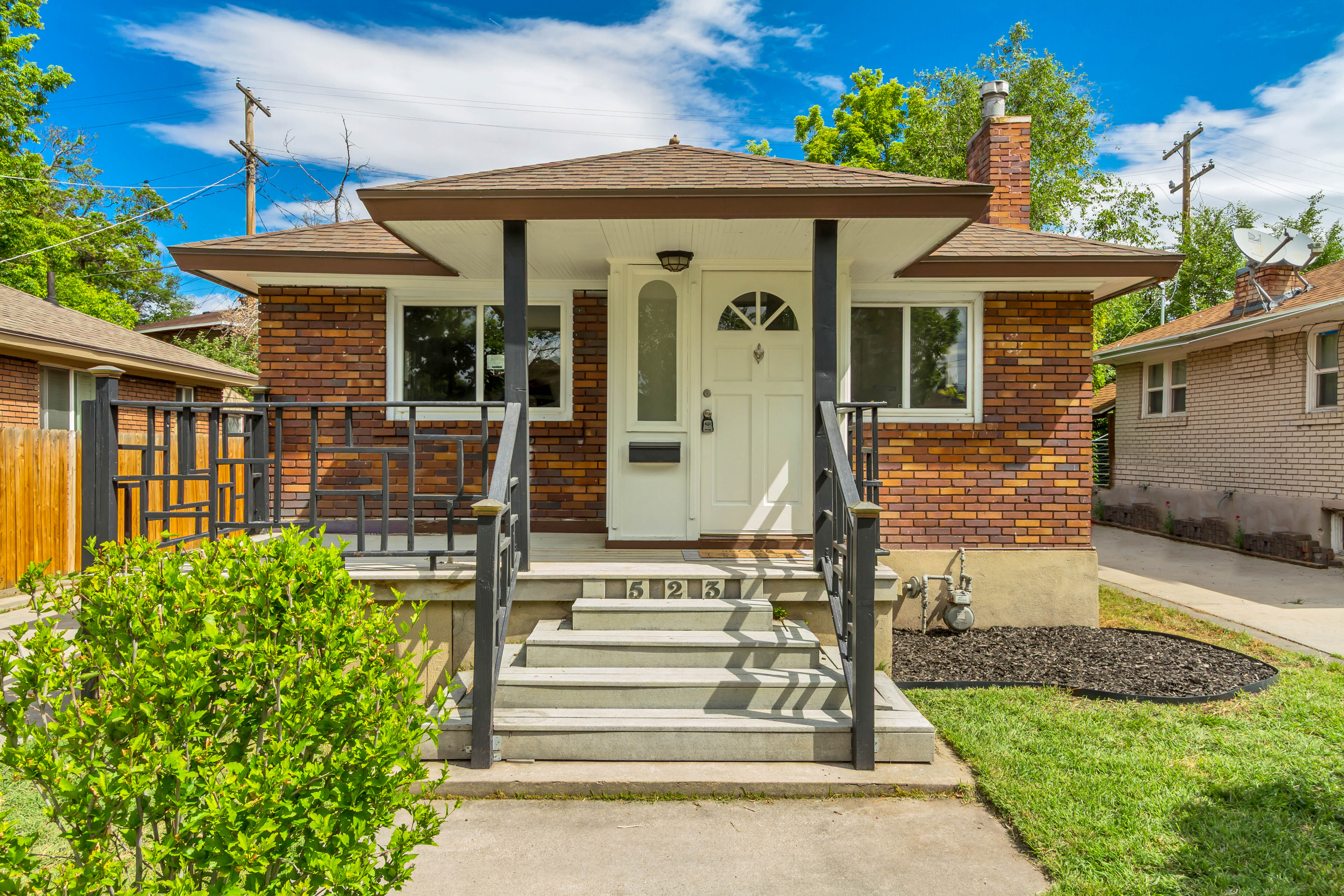 Brick exterior featuring a covered front porch with decorative railings, concrete steps, and a white entry door with an arched glass insert