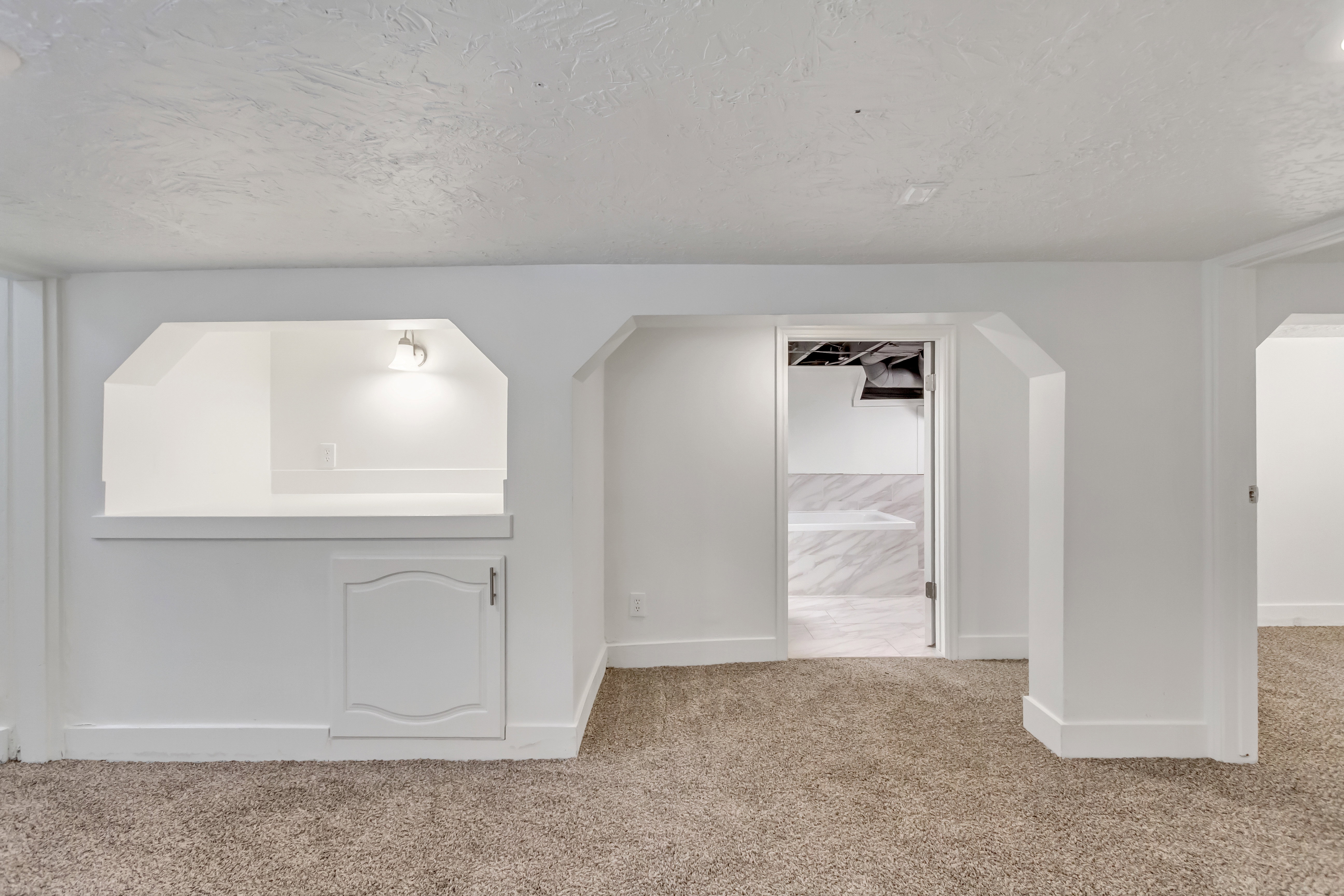 Carpeted room with a built-in white service bar featuring overhead lighting and a lower storage cabinet