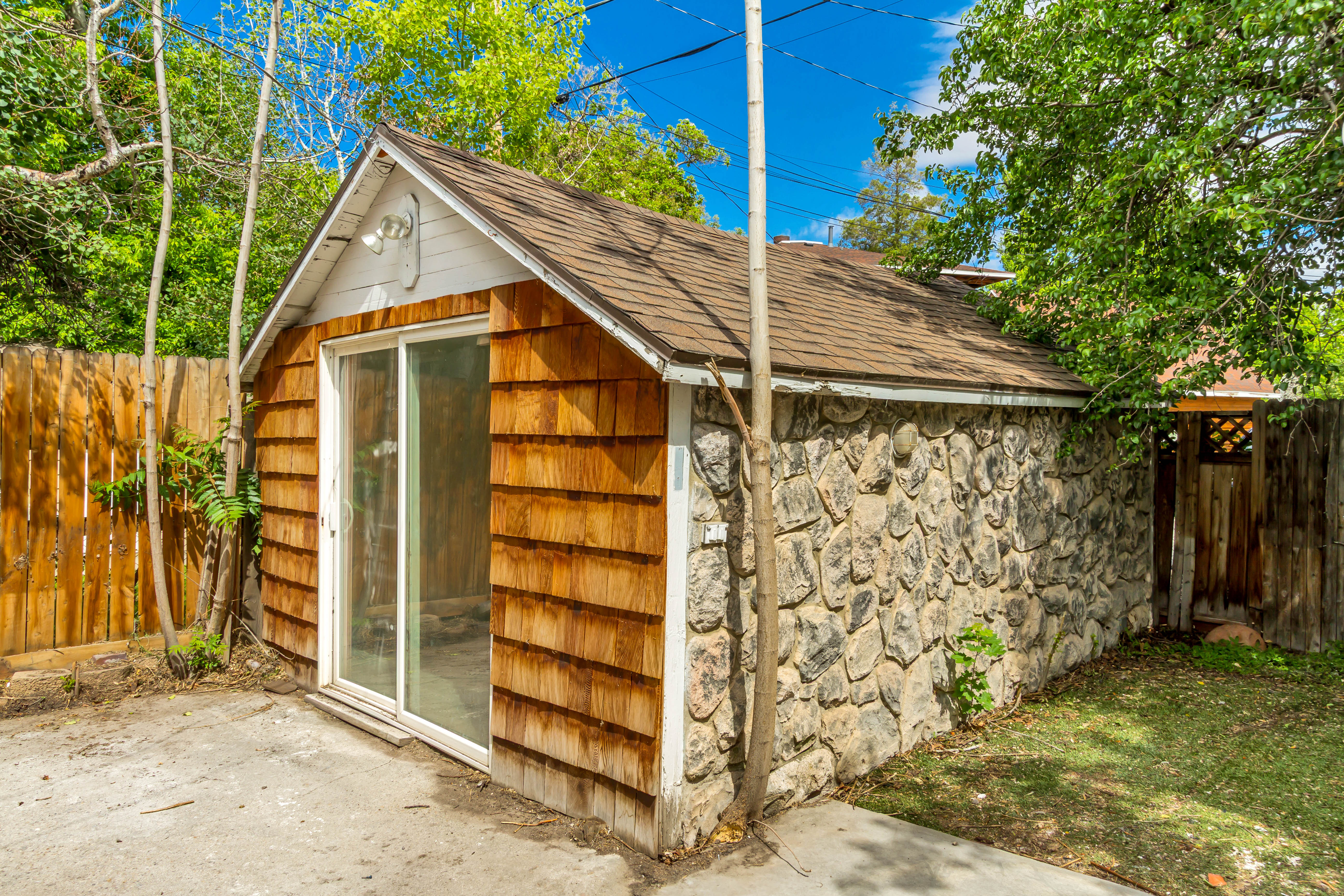 Detached structure featuring a shingle roof, stone and cedar shake siding, and sliding glass door