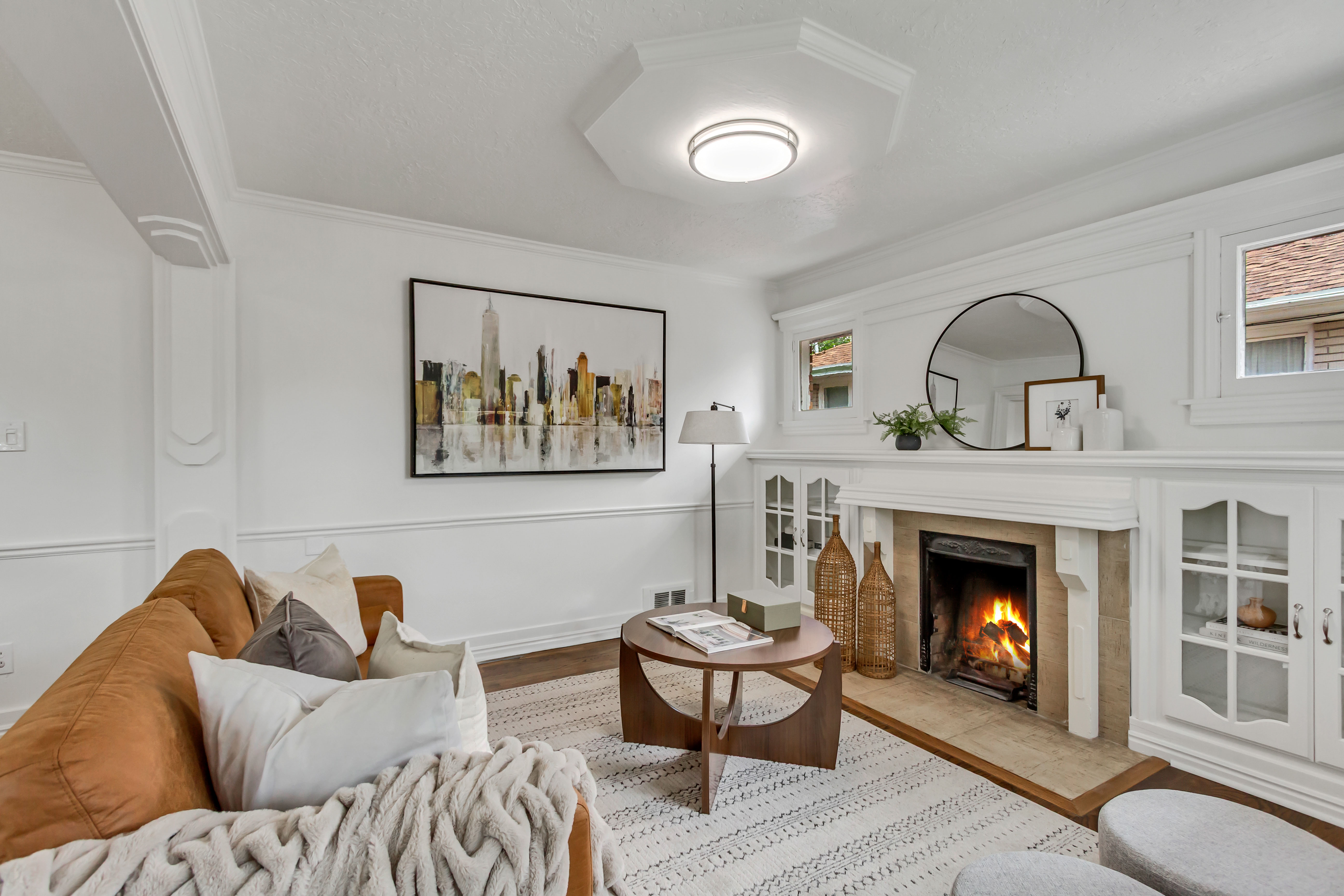 Living area featuring a fireplace with a stone surround, built-in cabinetry with glass-front doors, crown molding, and wood-finish flooring