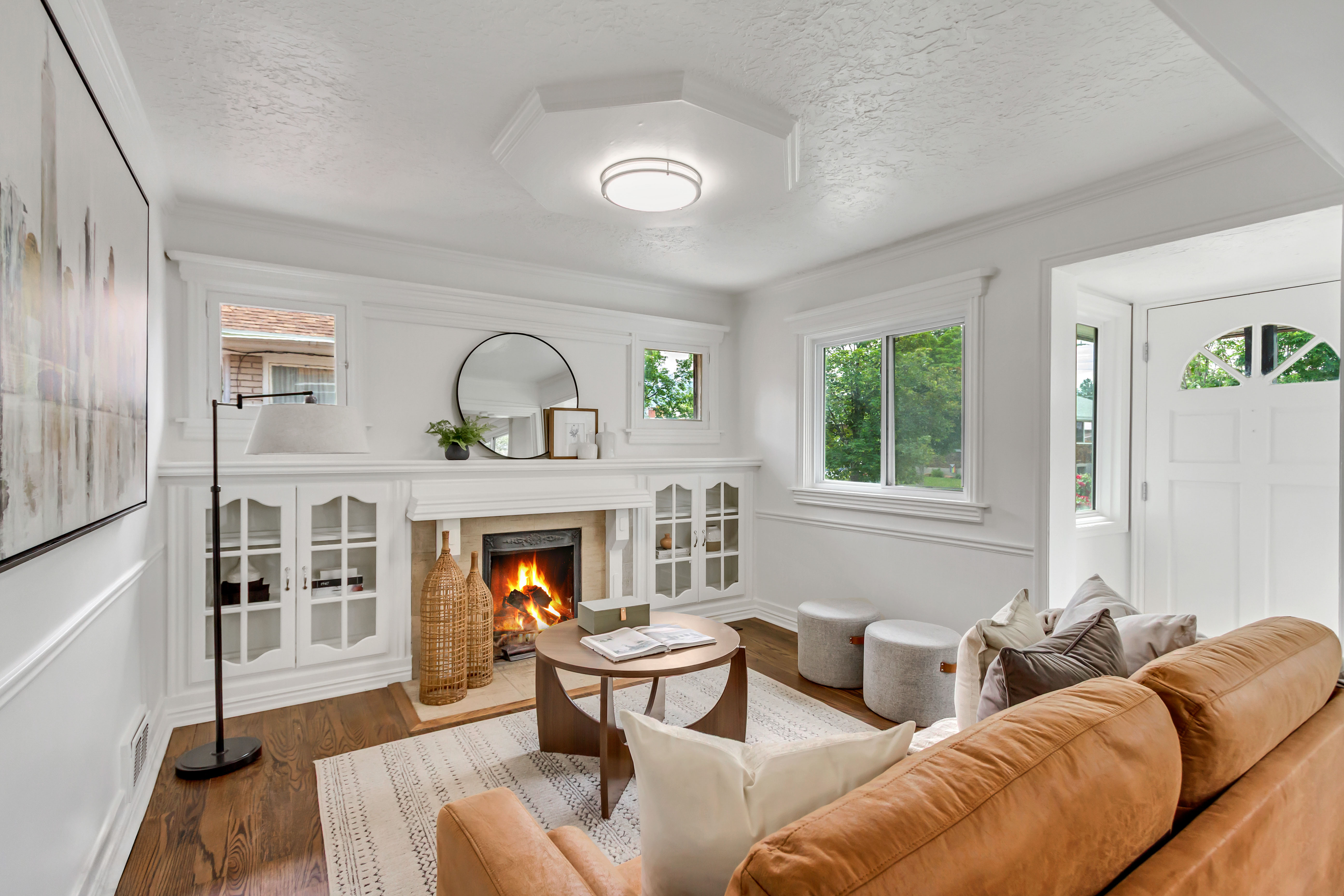 Living room featuring a fireplace with built-in cabinetry, wood-finish flooring, white trim, and a decorative front entry door with an arched window