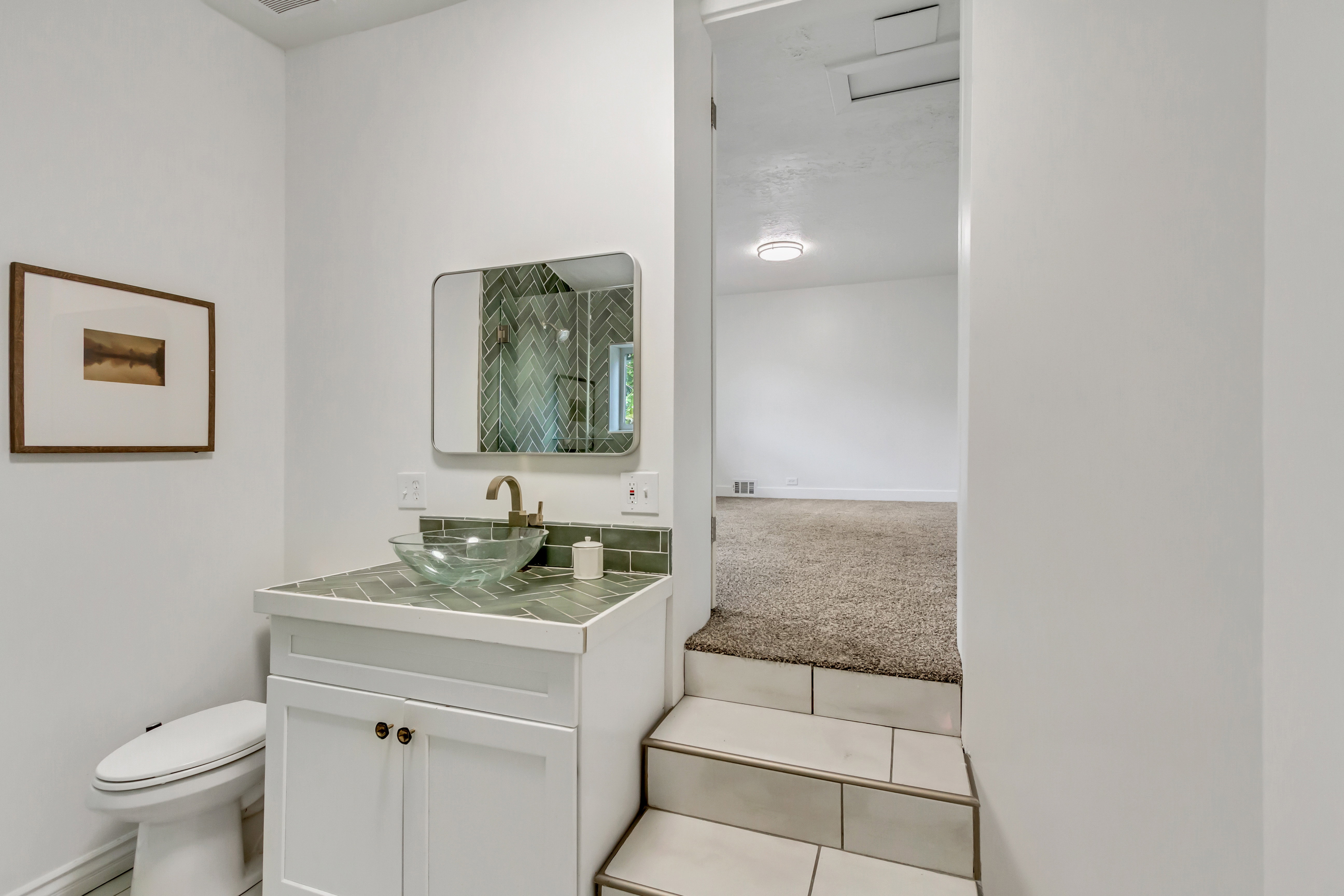 Bathroom vanity featuring a vessel sink, herringbone tile backsplash, white cabinetry, and a wall-mounted mirror