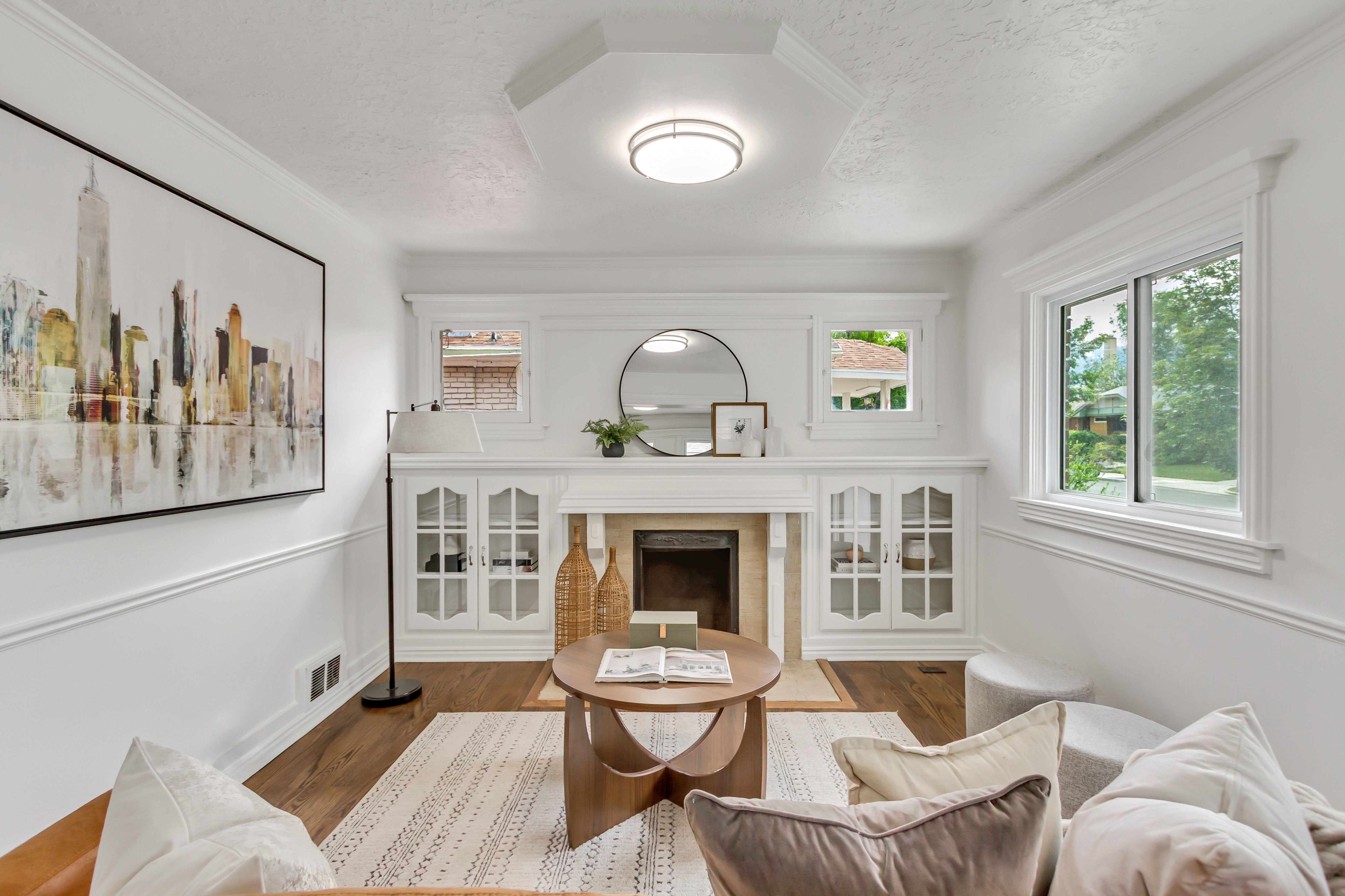Living area featuring a fireplace with a light-colored surround, built-in cabinetry with glass-front doors, and wood-finish flooring