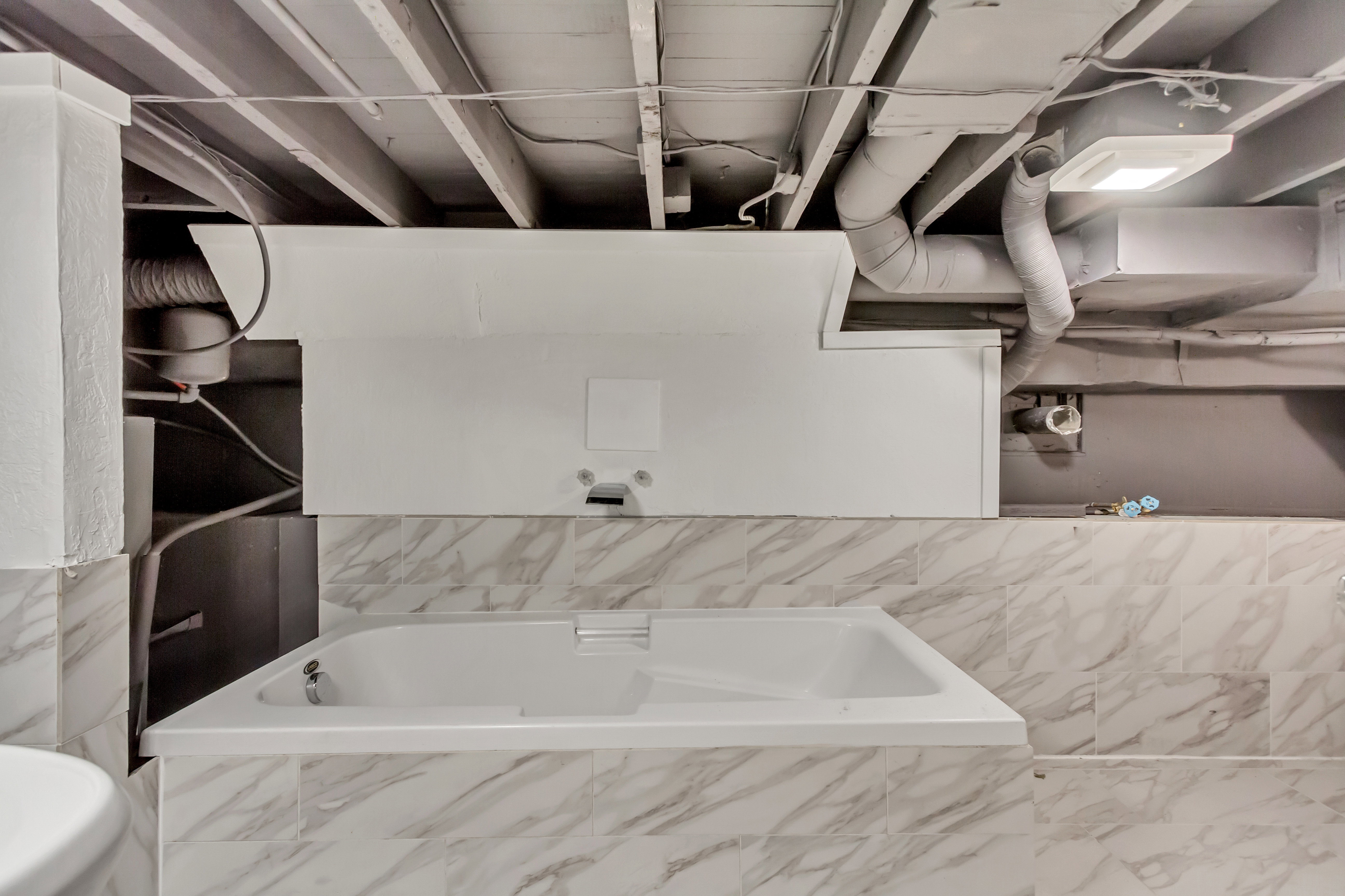 Built-in soaking tub with a white finish, surrounded by marble-look wall tiling