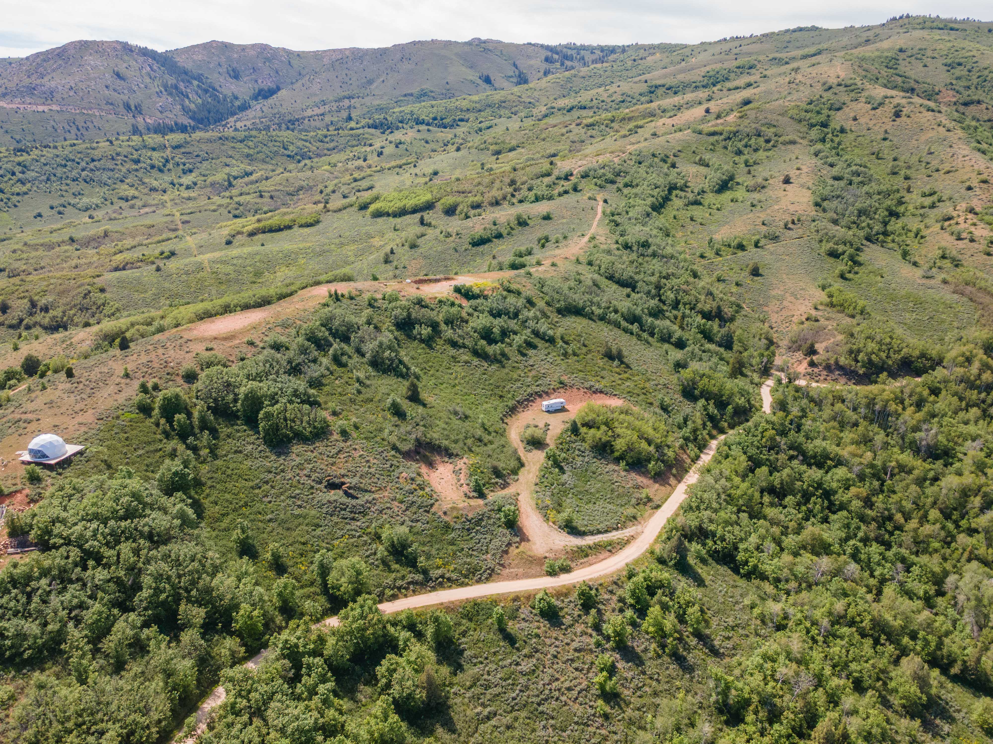 Expansive mountainous terrain featuring diverse green foliage and visible dirt roads