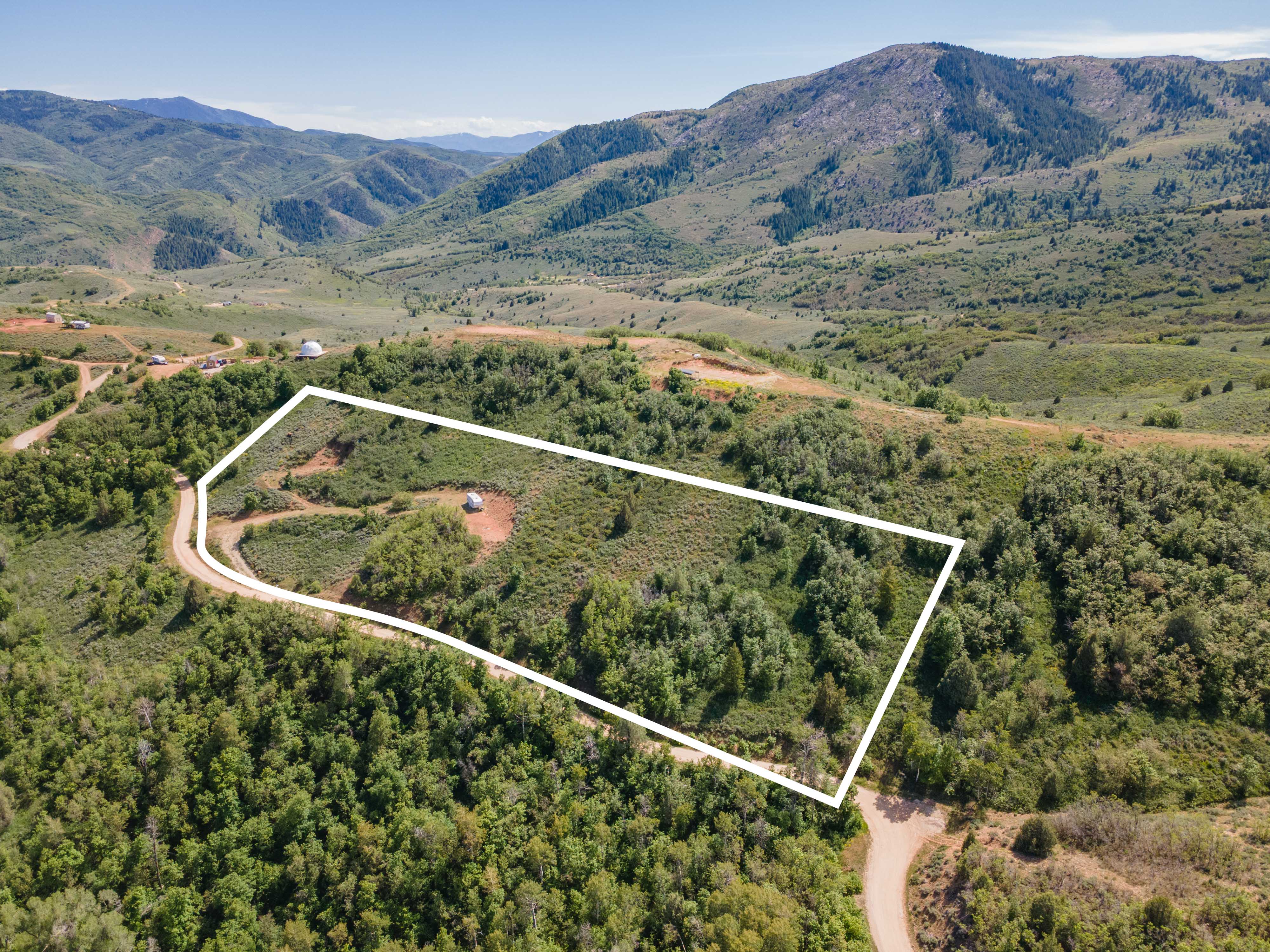 Expansive mountain property featuring dense tree coverage, a natural clearing, and a winding dirt road