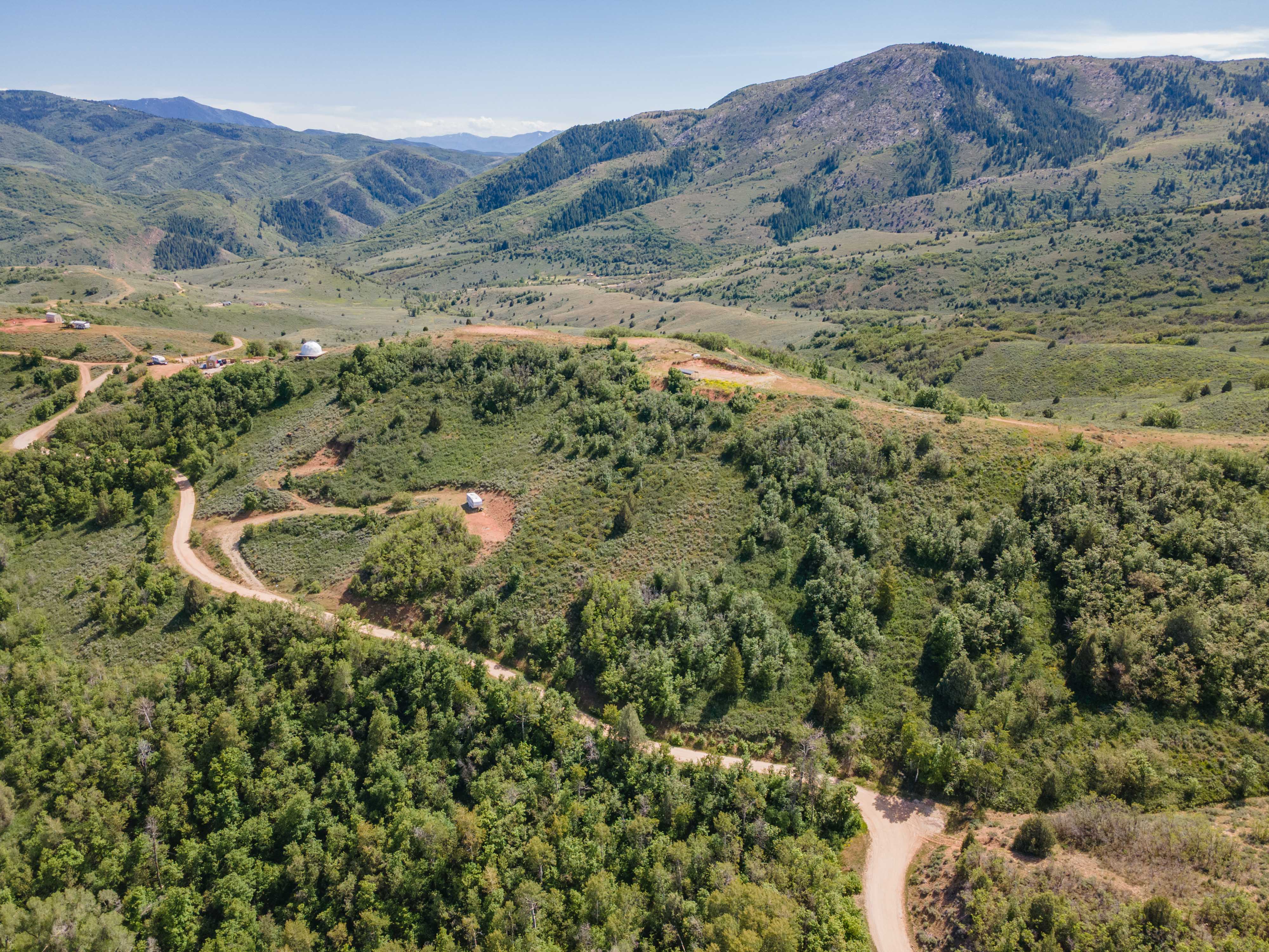 Expansive mountainous landscape featuring lush green foliage and winding unpaved roads