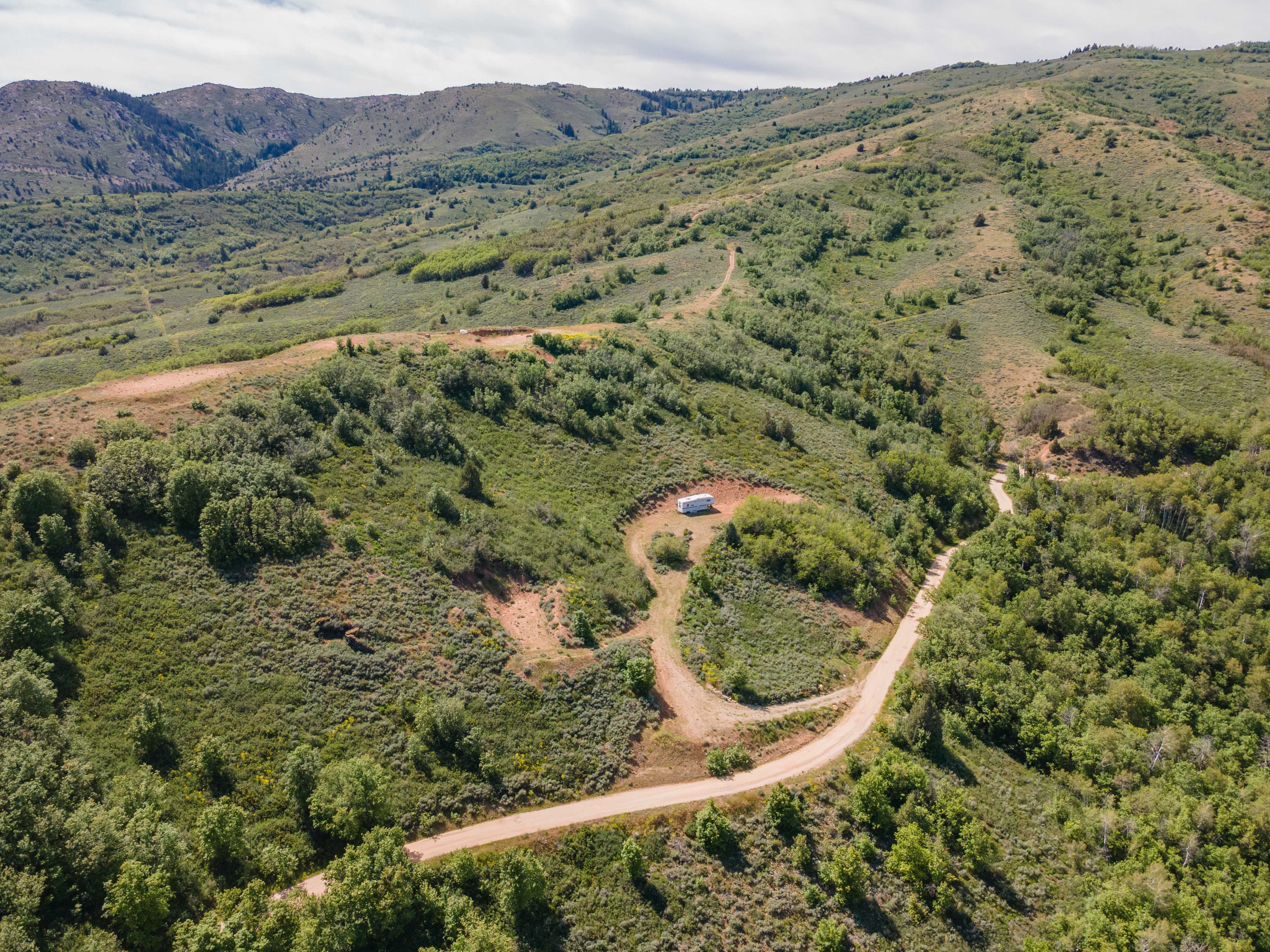 Expansive mountainous terrain featuring a winding dirt road and extensive tree coverage