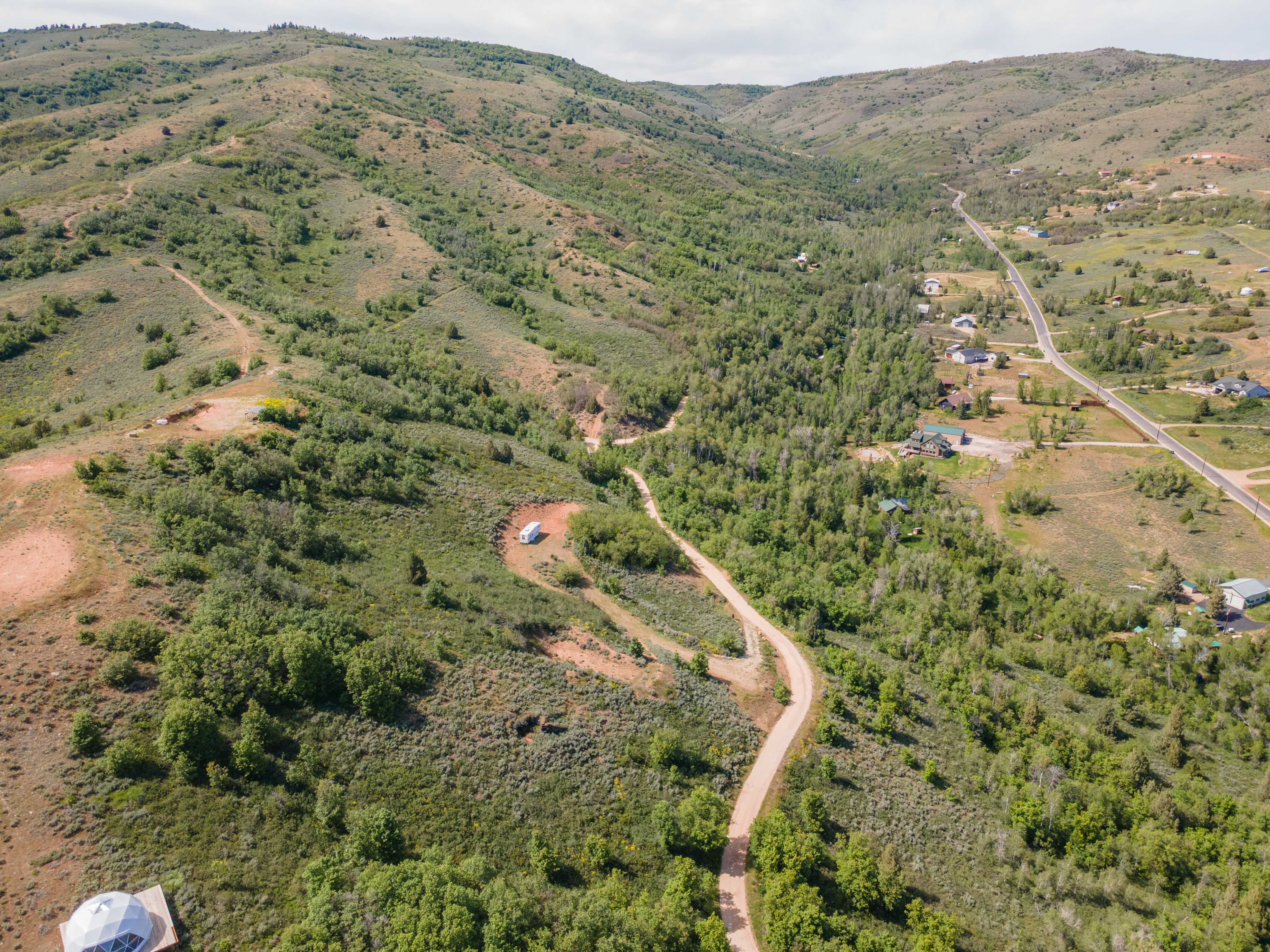 Expansive mountain terrain featuring a winding unpaved road, scattered evergreen trees, and distant homes
