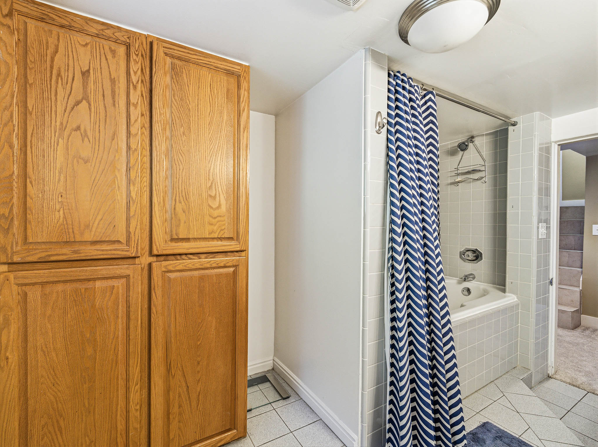 Built-in wood-finish cabinetry providing ample storage, a full-size tub, and tiled flooring