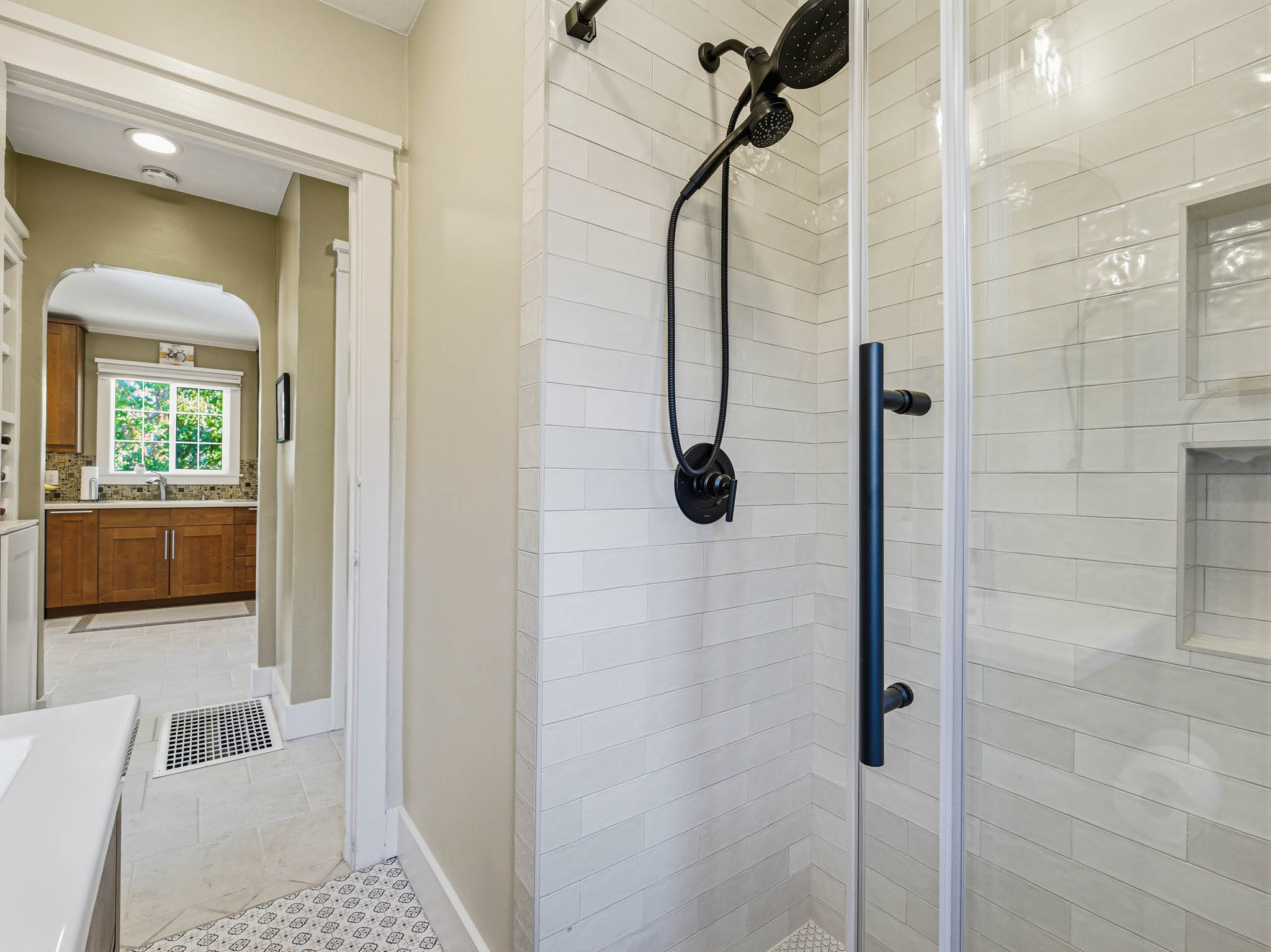 Glass-enclosed shower featuring white subway tile, integrated shelving, and matte black fixtures