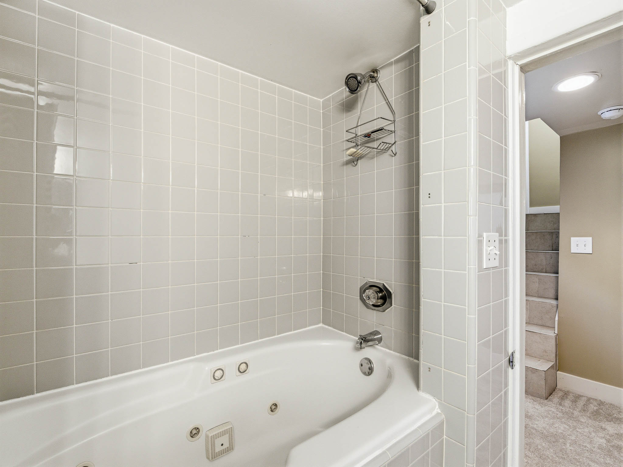 Corner jetted tub surrounded by light-toned square wall tiles