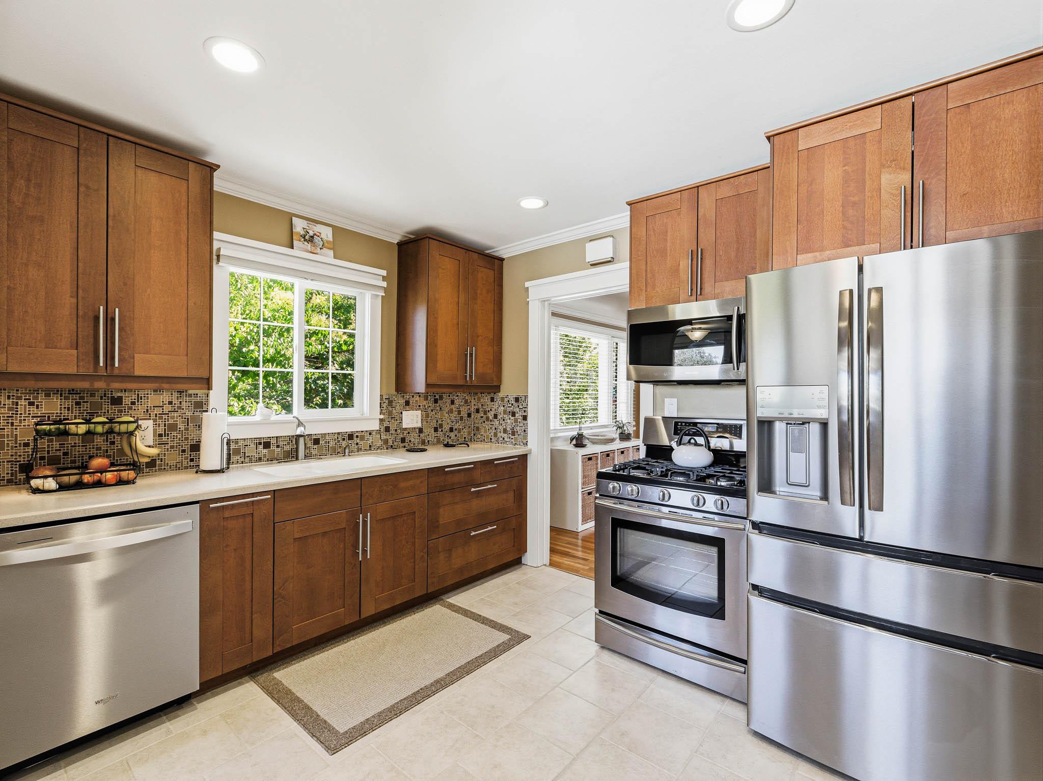 Kitchen featuring warm wood cabinetry, stainless steel appliances, a mosaic tile backsplash, light-toned countertops, and recessed lighting