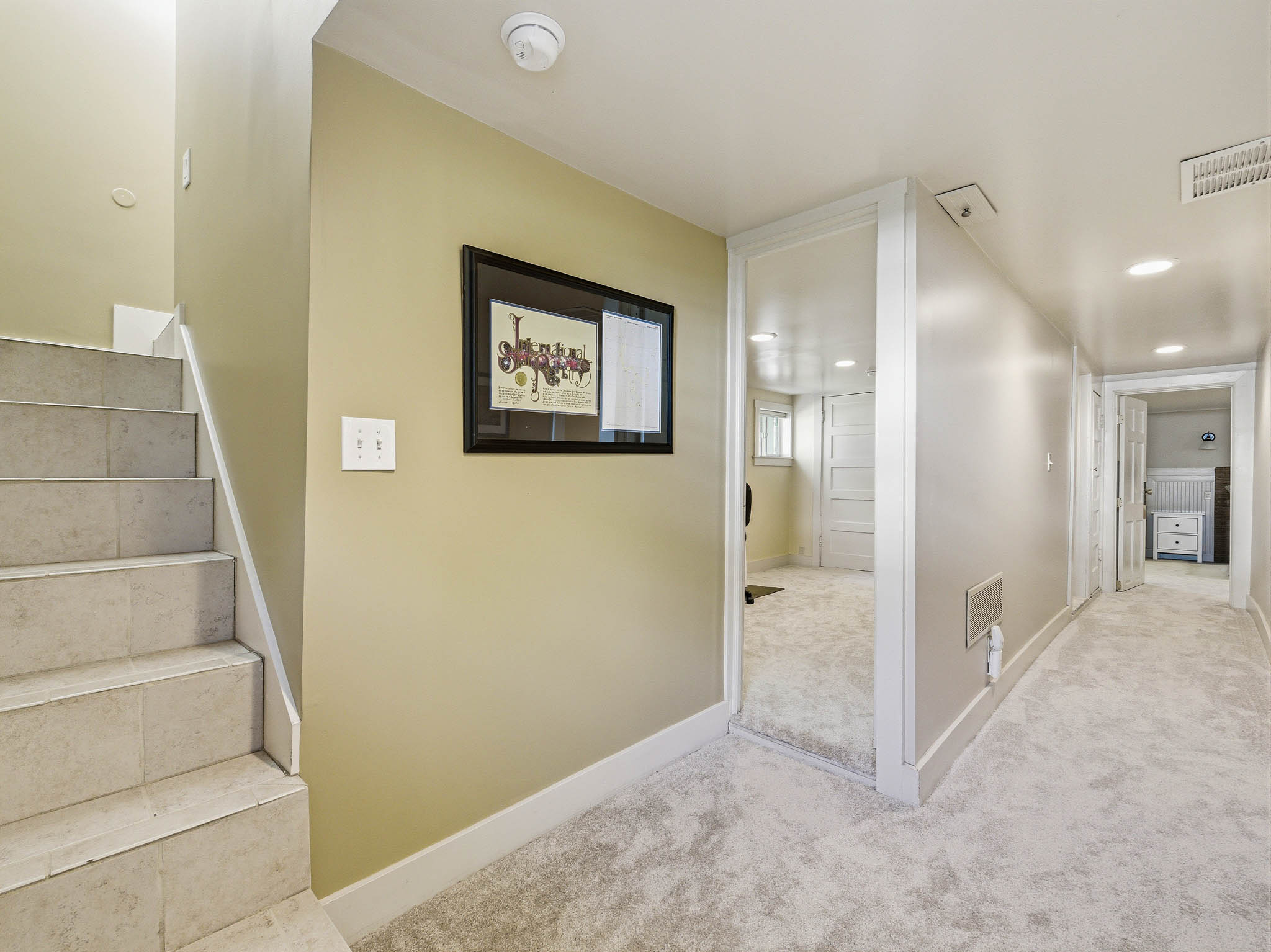 Carpeted hallway with recessed lighting, an open doorway, and a tiled staircase