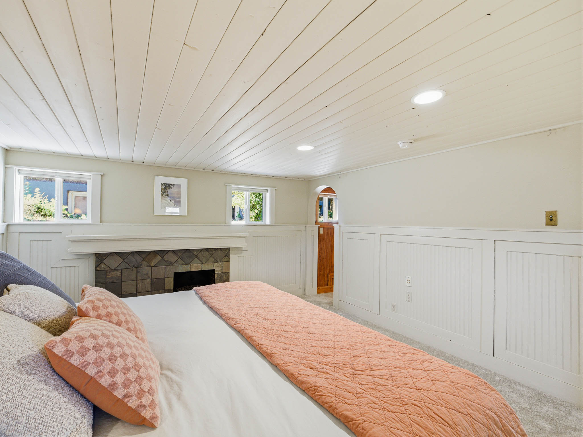 Interior room featuring a stone-faced fireplace with a white mantel, two windows, wainscoting, and a wood-finish door