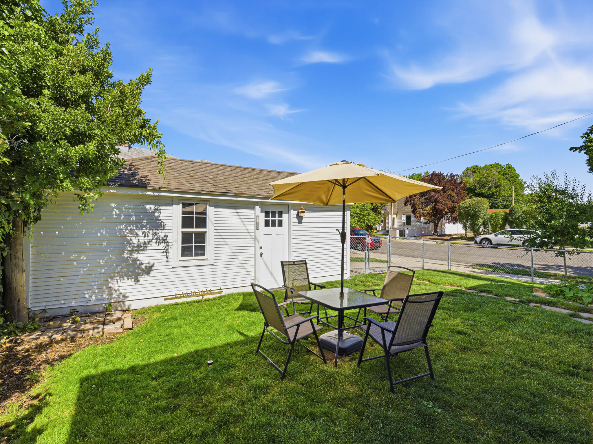 Expansive grassy yard area alongside a white-sided outbuilding with a single window and exterior door, all enclosed by chain-link fencing