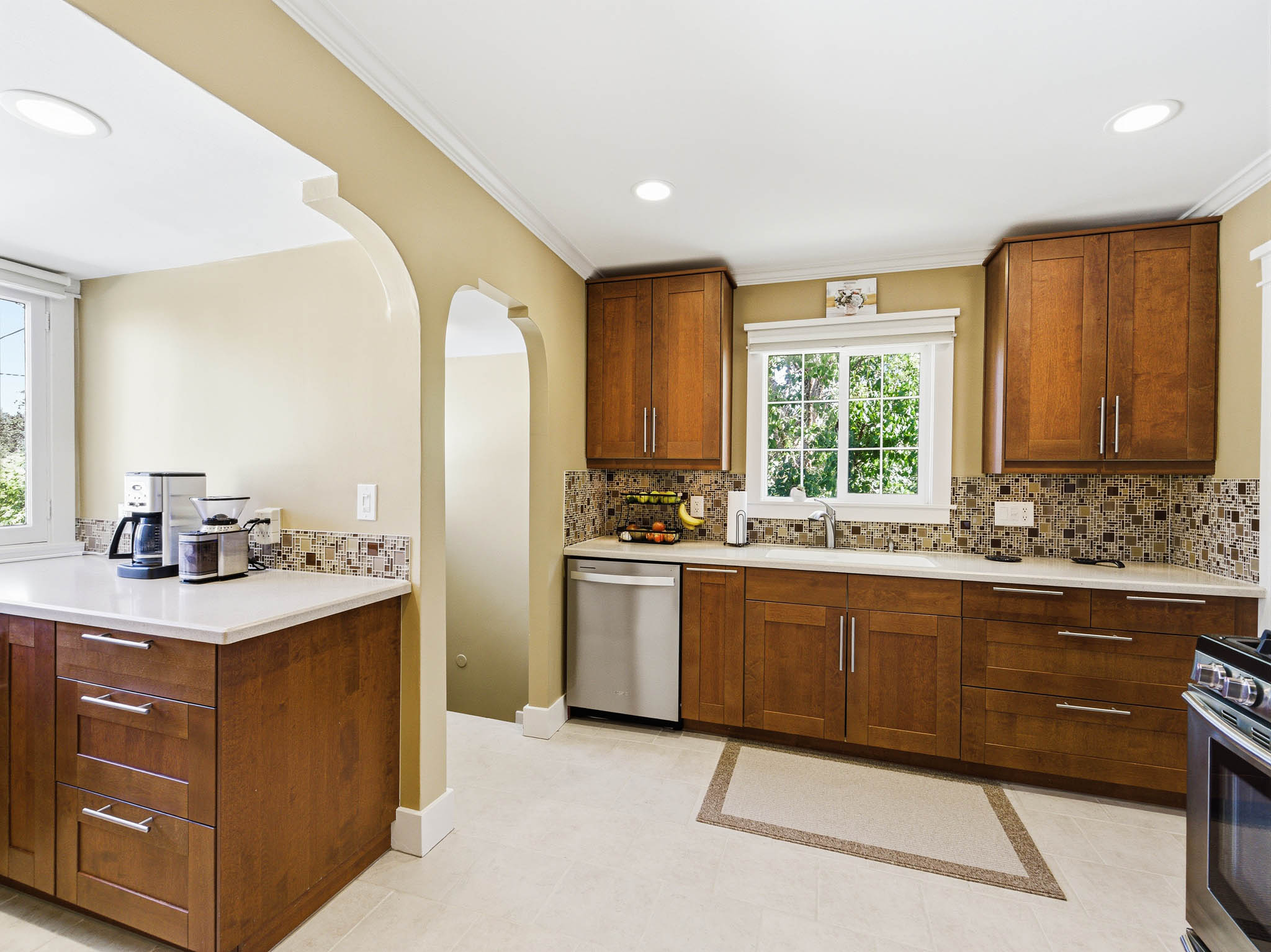 Kitchen featuring wood cabinetry, light-toned countertops, a mosaic tile backsplash, stainless steel appliances, and tile flooring with an accent border