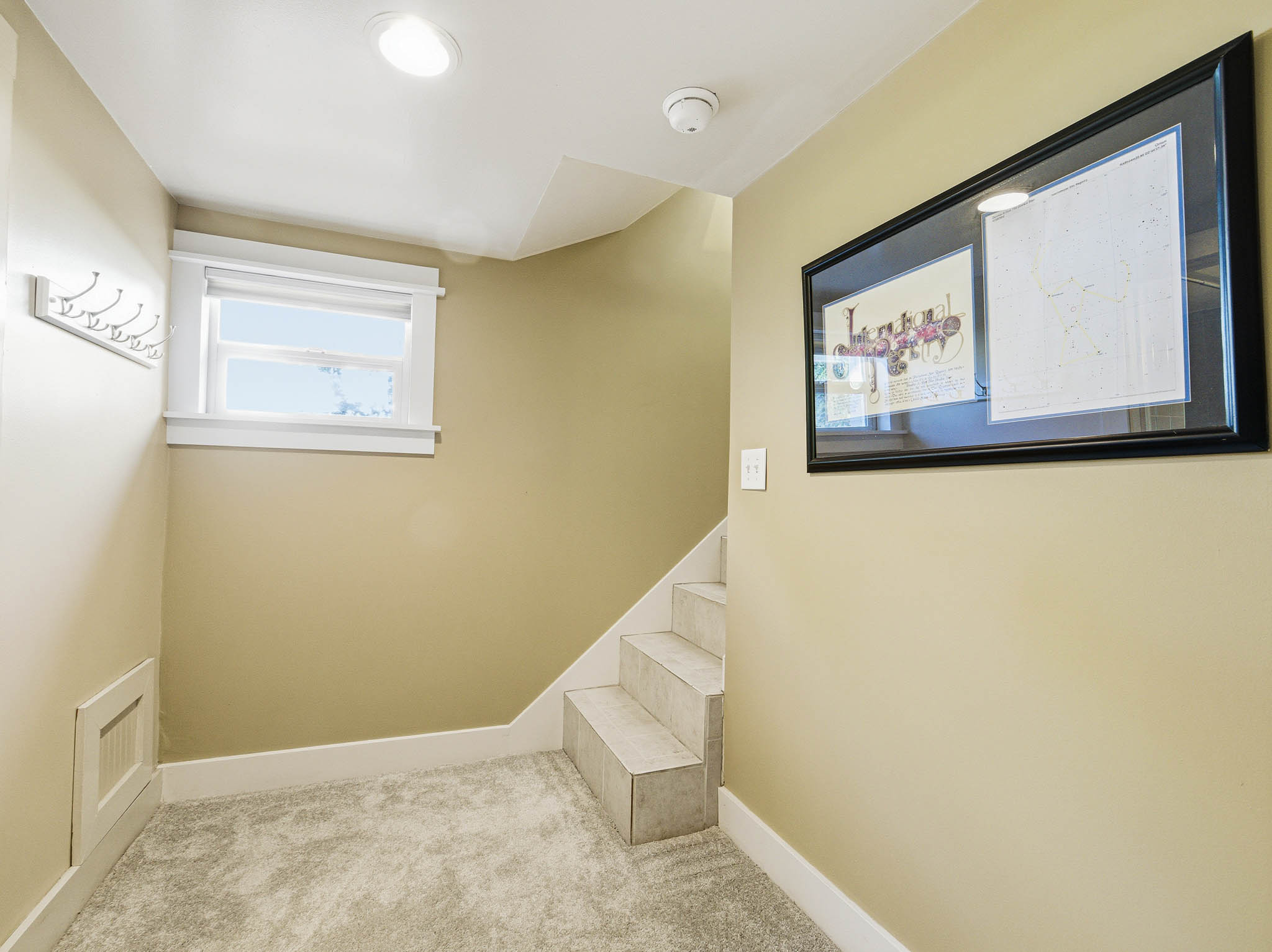 Lower level entry area featuring neutral wall paint, recessed lighting, a window with white trim, a coat rack, and carpeted flooring