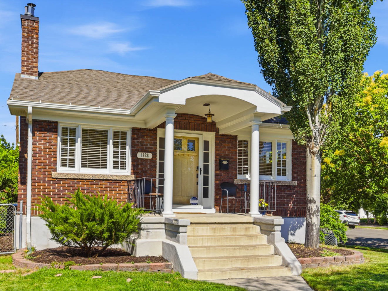 Brick-clad residence featuring a covered front porch with white columns, a multi-pane front window, and a prominent brick chimney