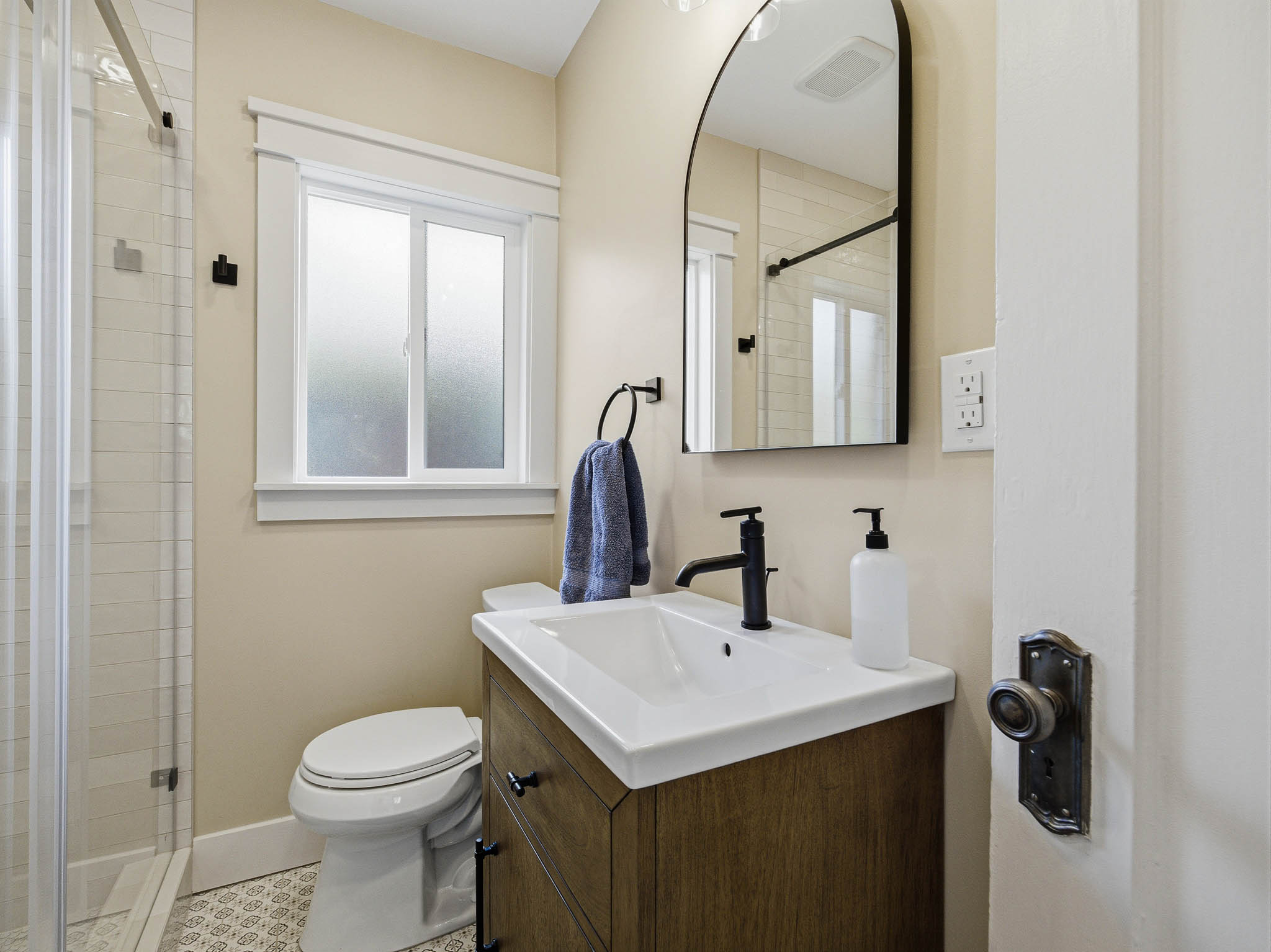 Bathroom featuring a wood-finish vanity with a white countertop, an arched black-framed mirror, and matte black fixtures