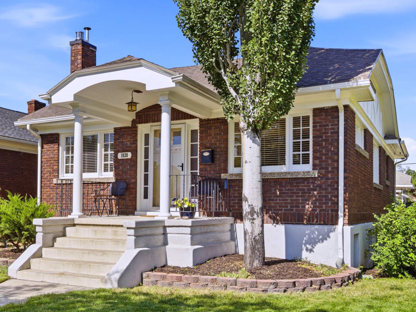 Brick exterior featuring a covered front porch with white columns, concrete steps, and a manicured lawn