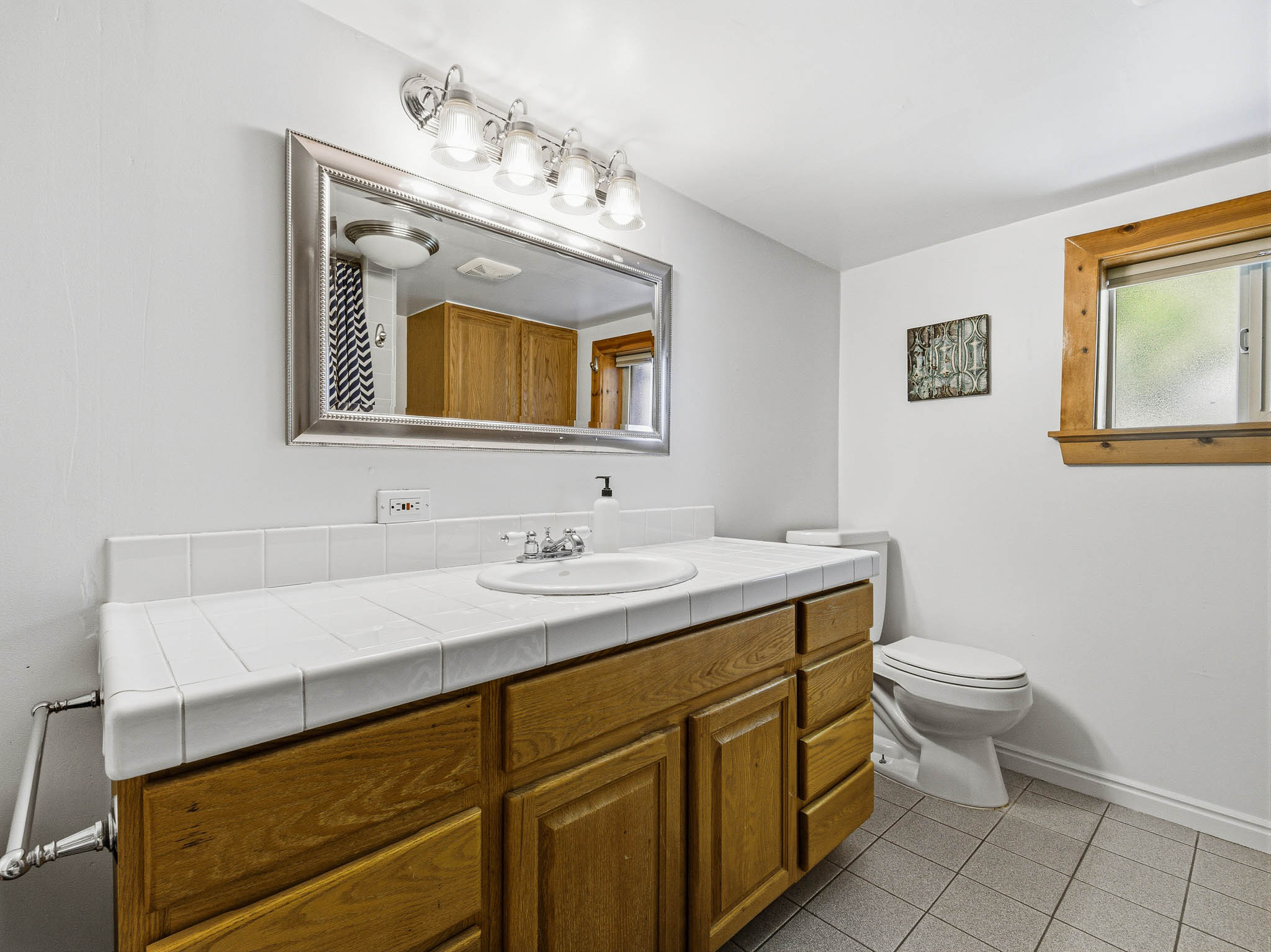 Bathroom featuring a wood-finish vanity with a tile countertop, integrated sink, and wall-mounted mirror with vanity lighting