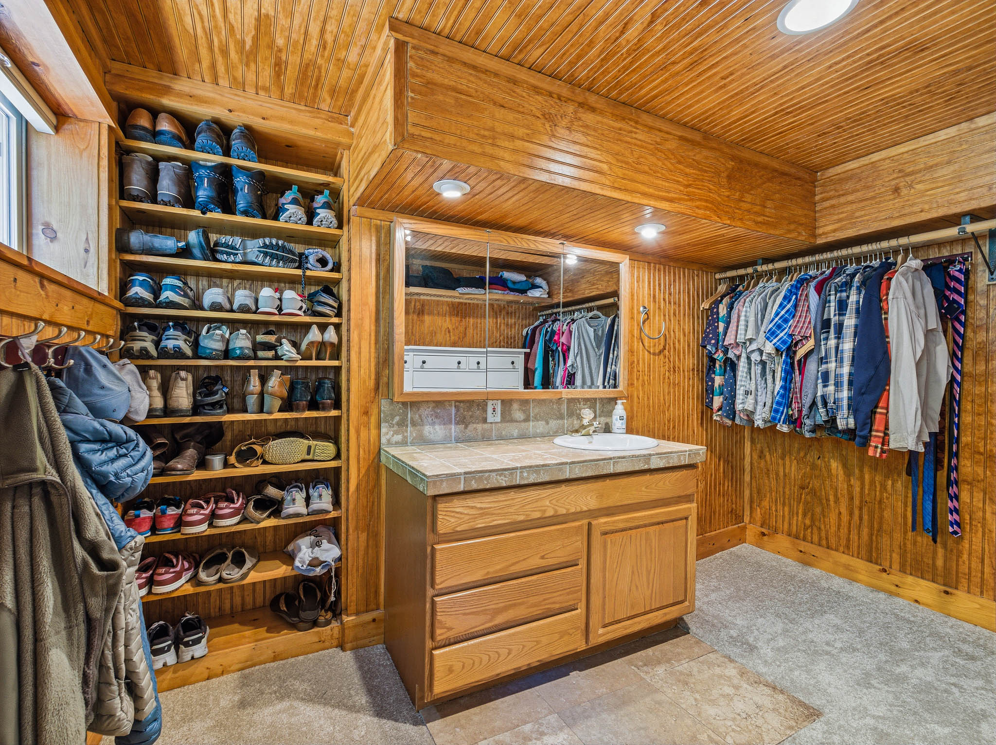 Walk-in closet featuring wood paneling, built-in shelving, a wood vanity with an integrated sink and laminate countertop, and overhead lighting