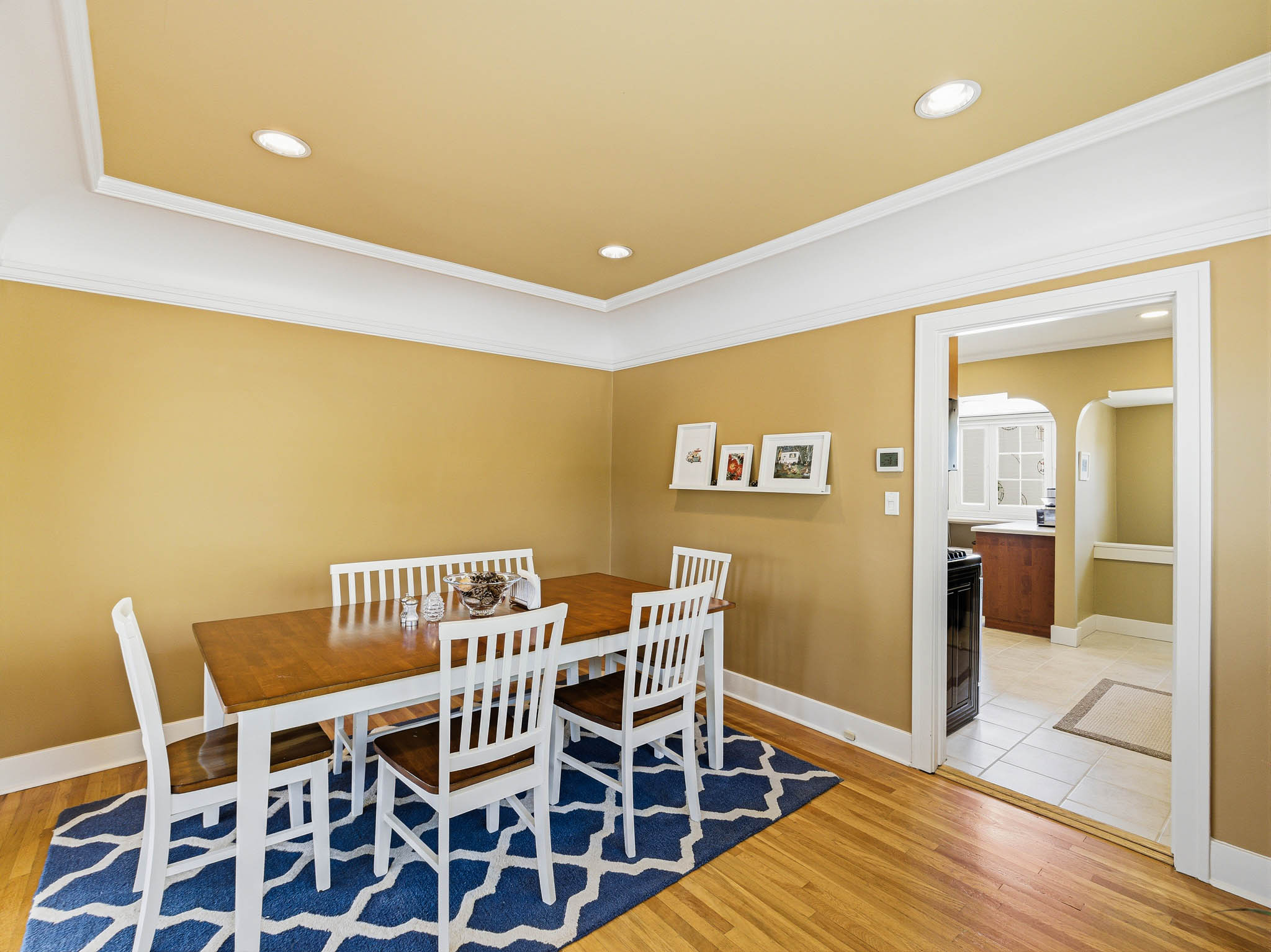 Hardwood flooring extending throughout, recessed lighting in the ceiling, a coved ceiling detail, and a doorway with wood trim opening to a tiled area