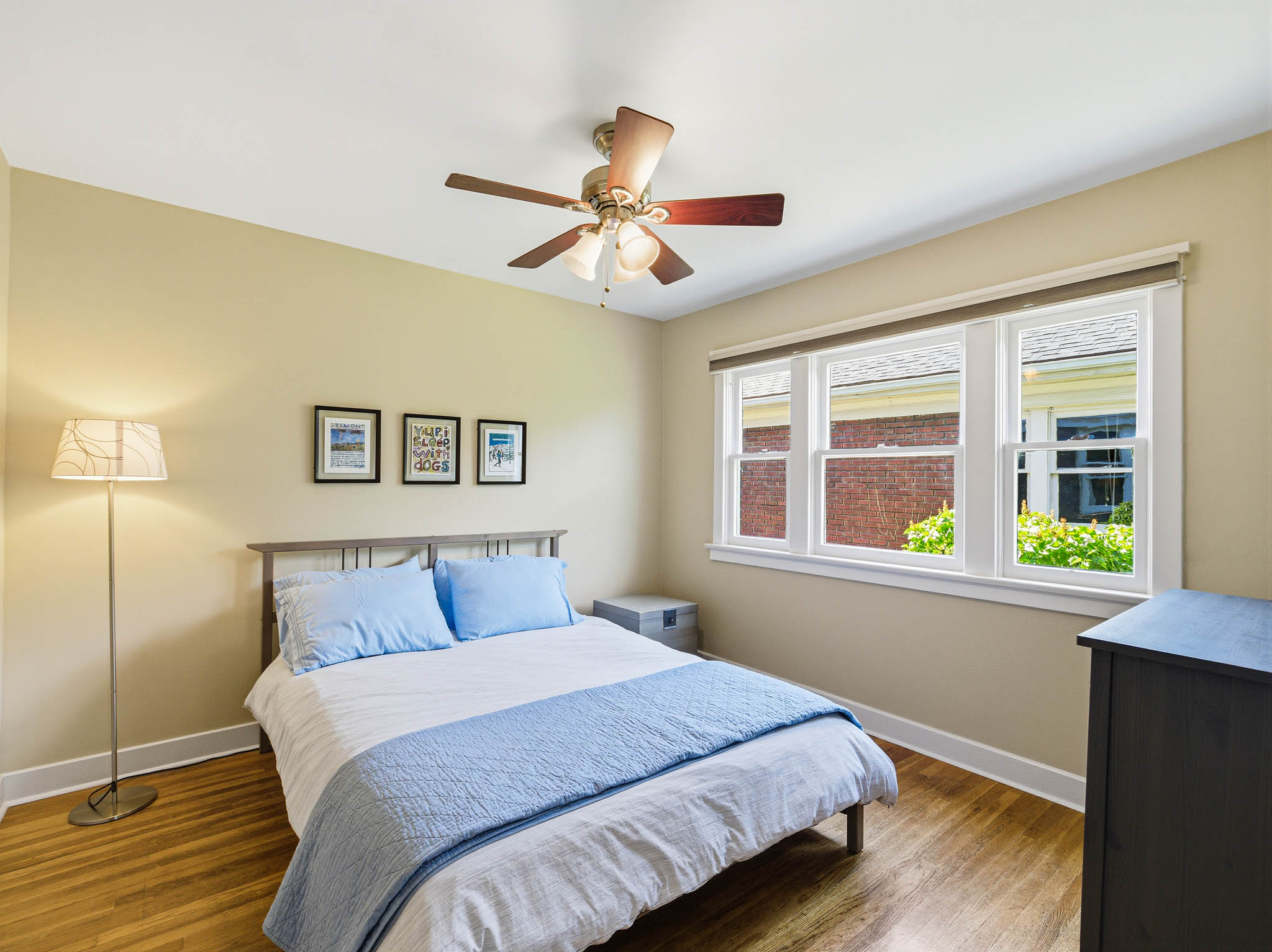 Room featuring wood-finish flooring, a three-panel window with white trim, and a ceiling fan with integrated lighting