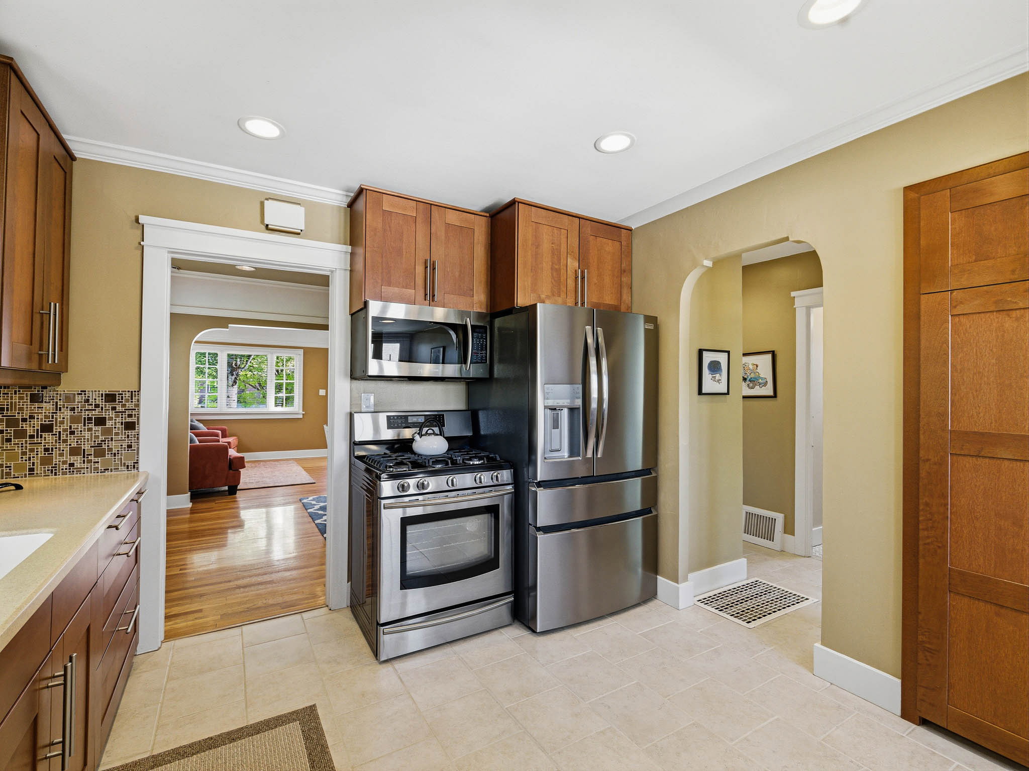 Kitchen featuring stainless steel appliances, wood cabinetry, tile flooring, and a mosaic tile backsplash