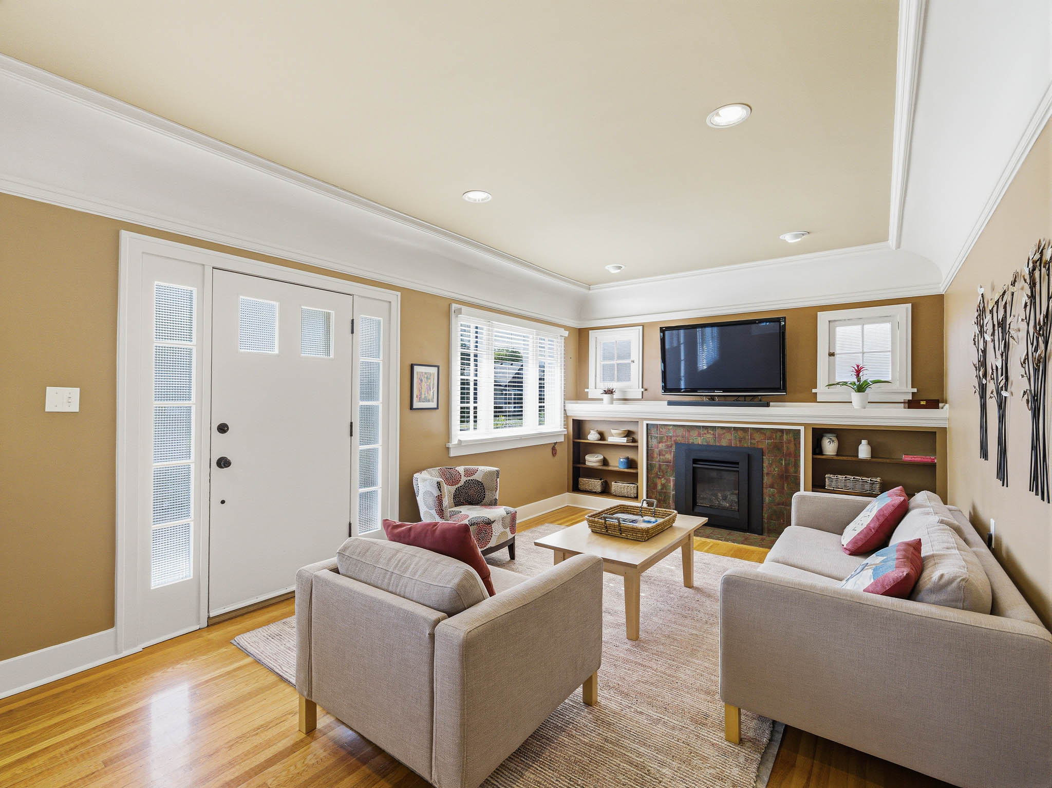 Living room featuring a tiled fireplace with built-in shelving, hardwood flooring, recessed lighting, and crown molding