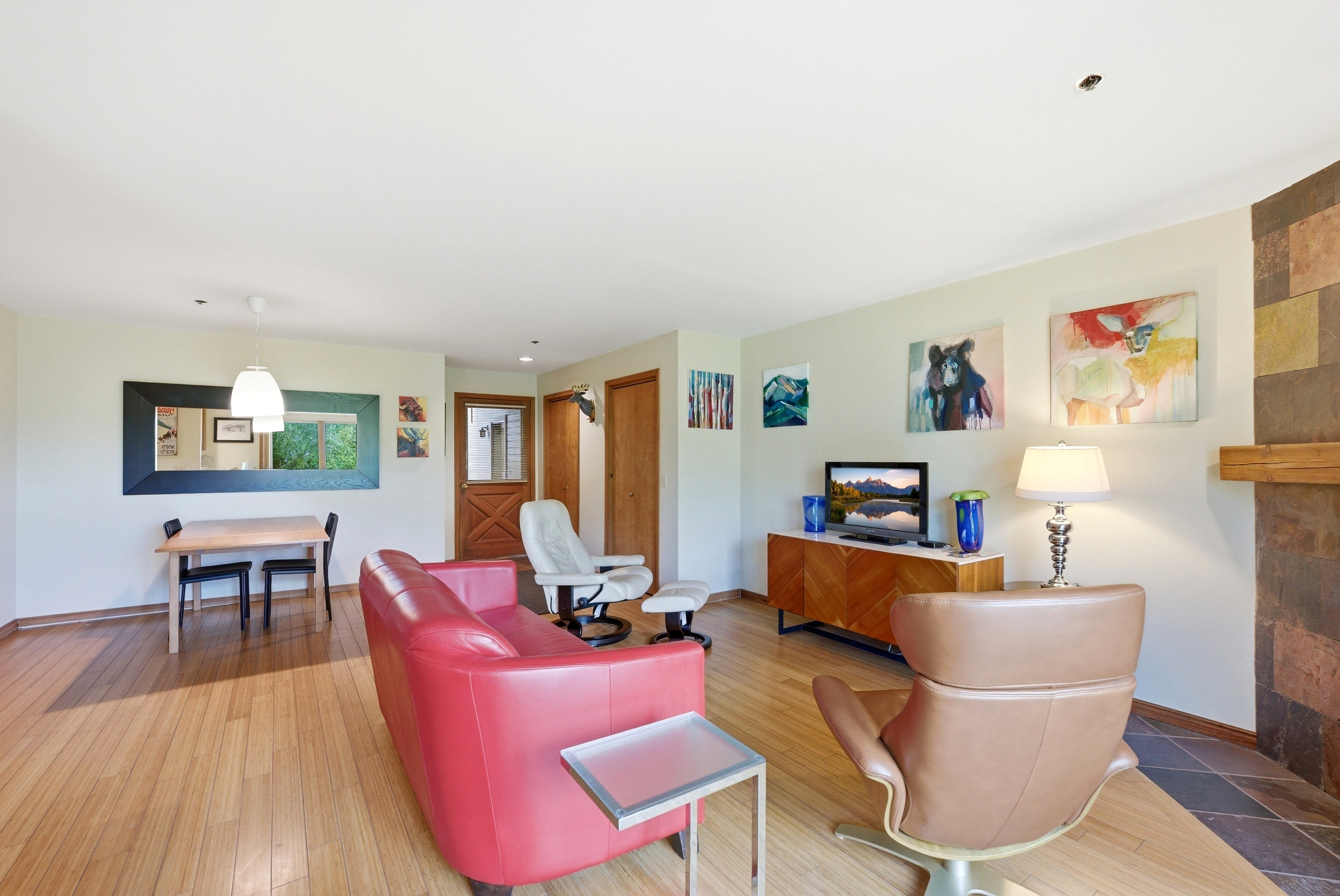 Open living area featuring wood-finish flooring, a contemporary pendant light fixture, and a stone-clad fireplace