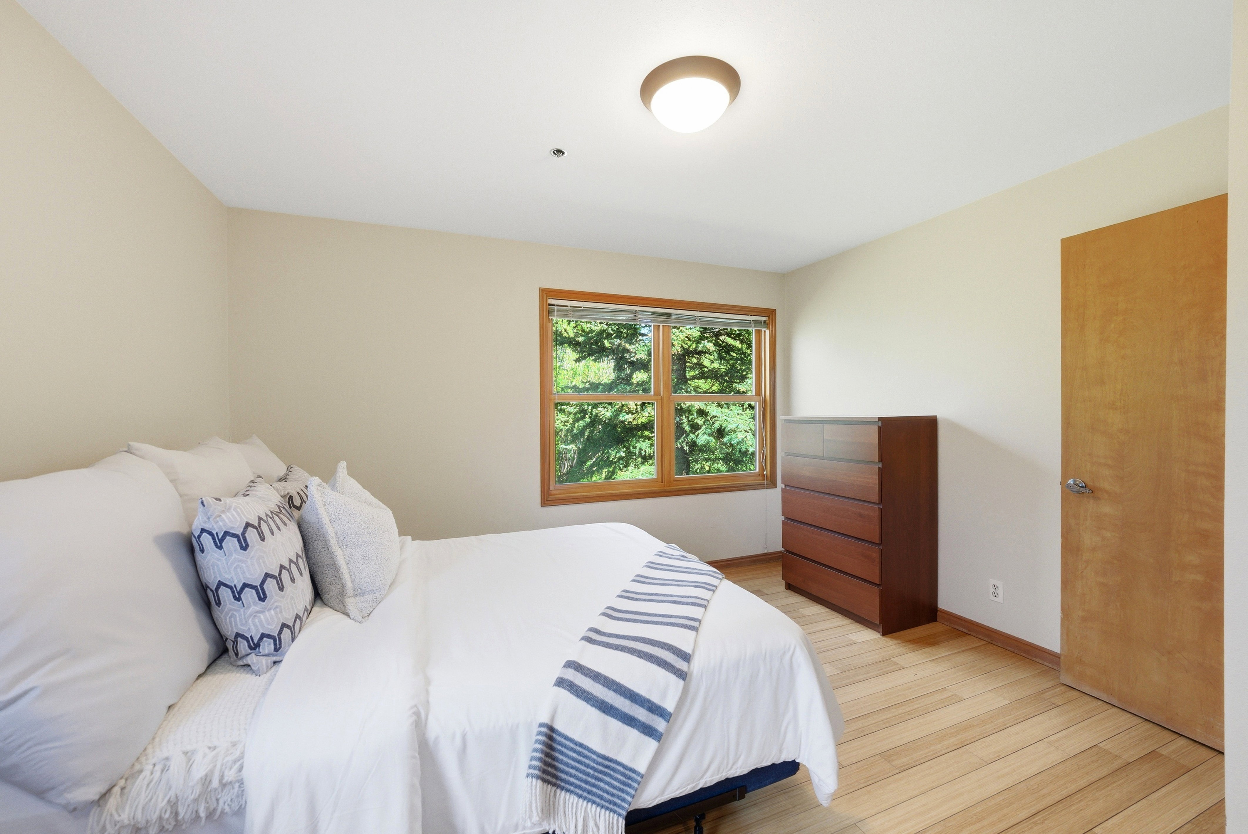 Bright room featuring wood-finish flooring, a window with wood trim, and a flush-mount ceiling light fixture