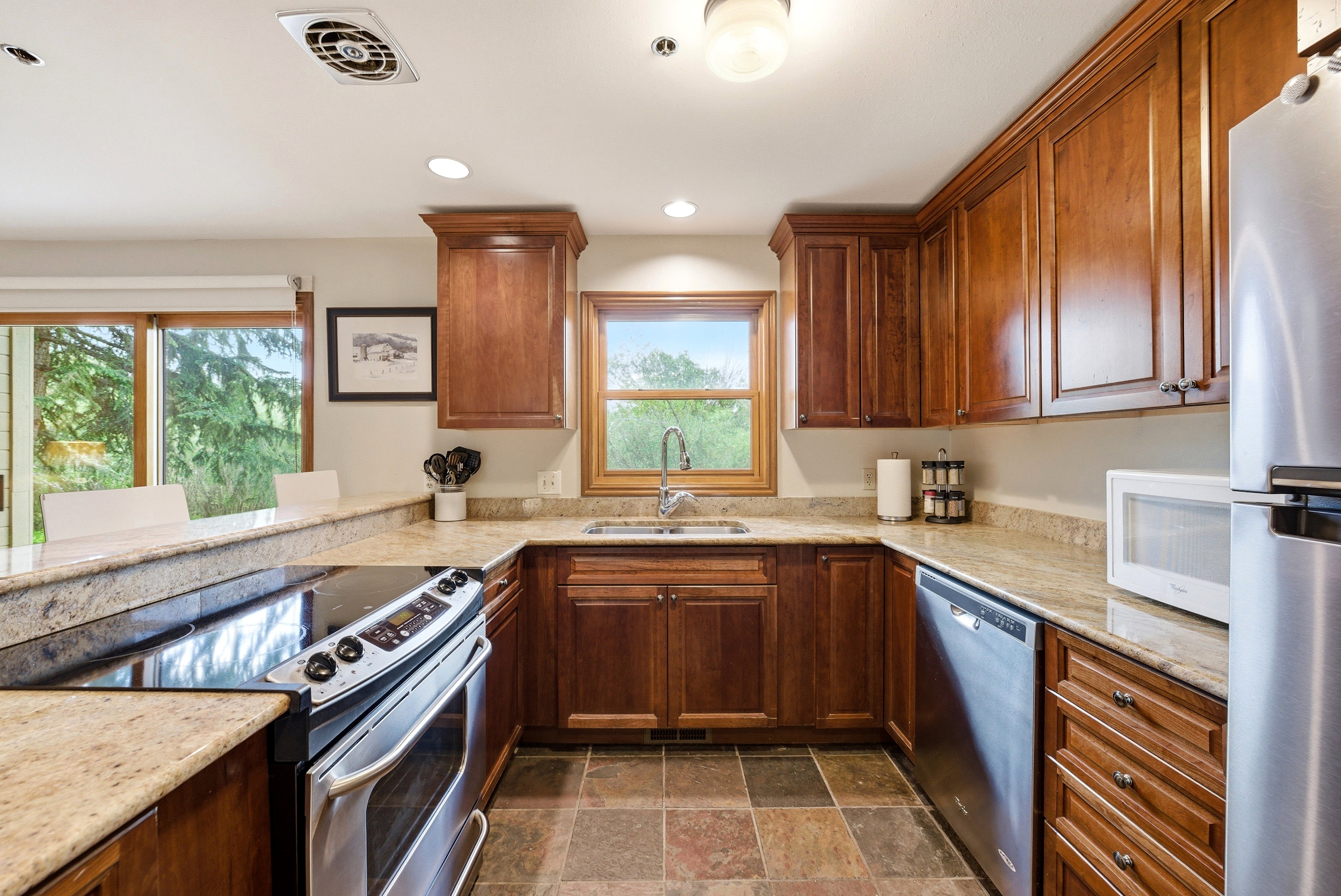 Kitchen featuring warm wood cabinetry, stone countertops, stainless steel appliances, and multi-toned tile flooring