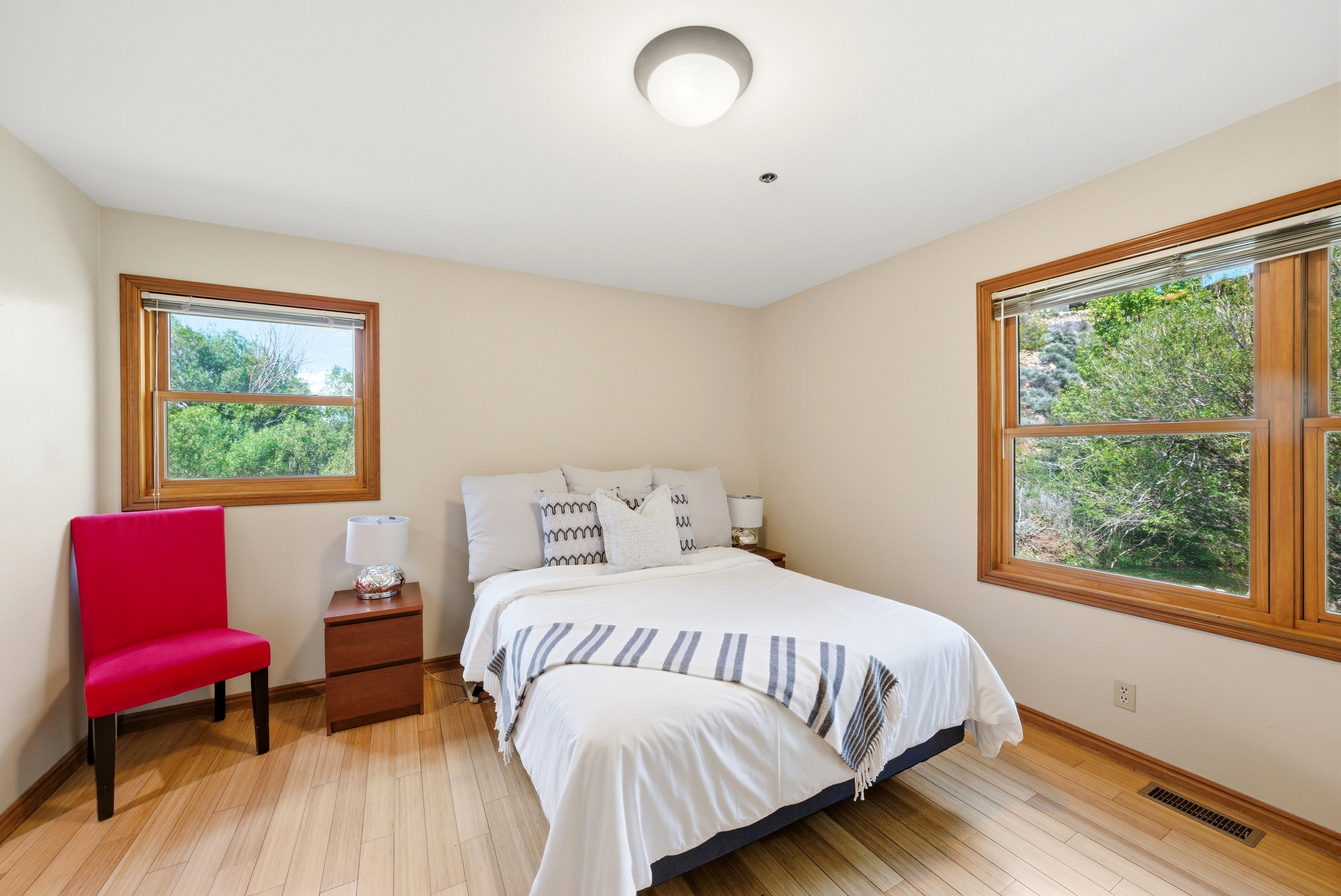 Bedroom featuring light wood-finish flooring, neutral wall tones, and two windows with wood frames